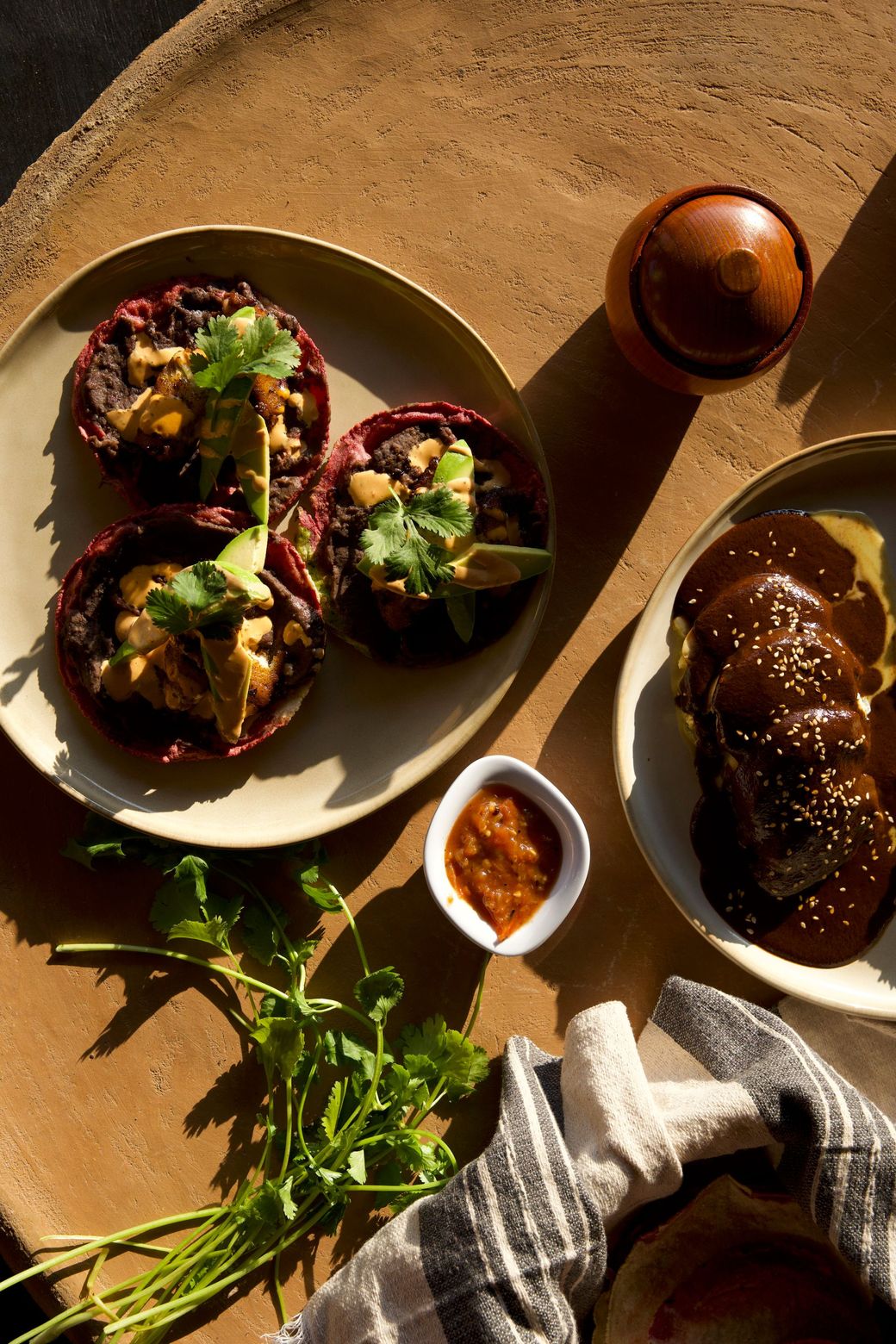 Three stuffed eggplants on a plate with herbs, sauce, and bread on a sunlit table