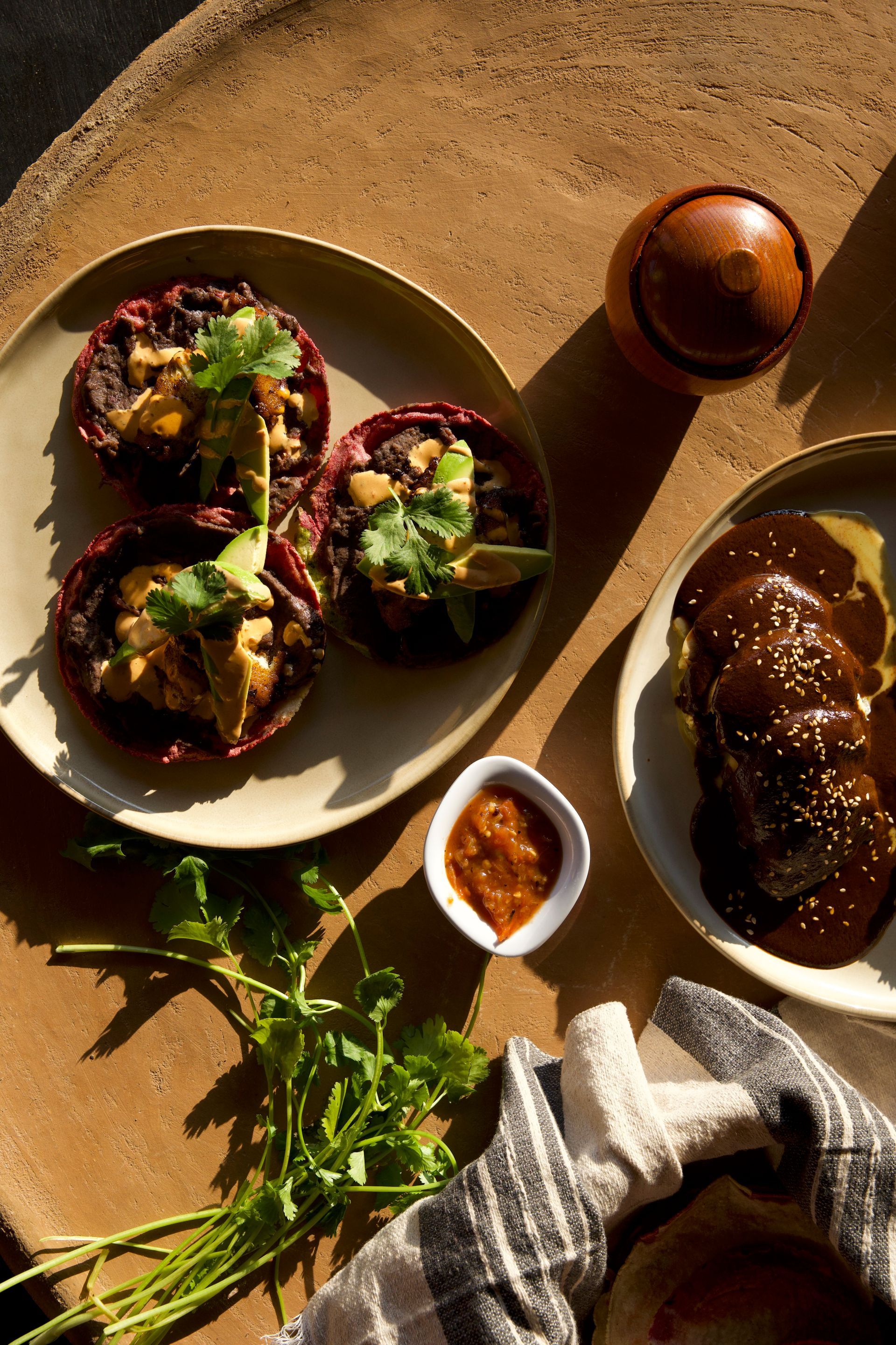 Three stuffed eggplants on a plate with herbs, sauce, and bread on a sunlit table