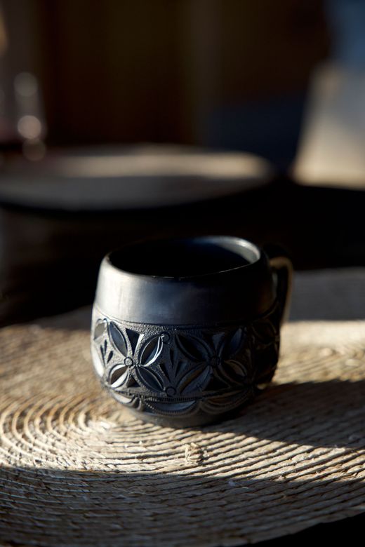 Black ceramic mug with embossed floral design on a woven tray in soft light