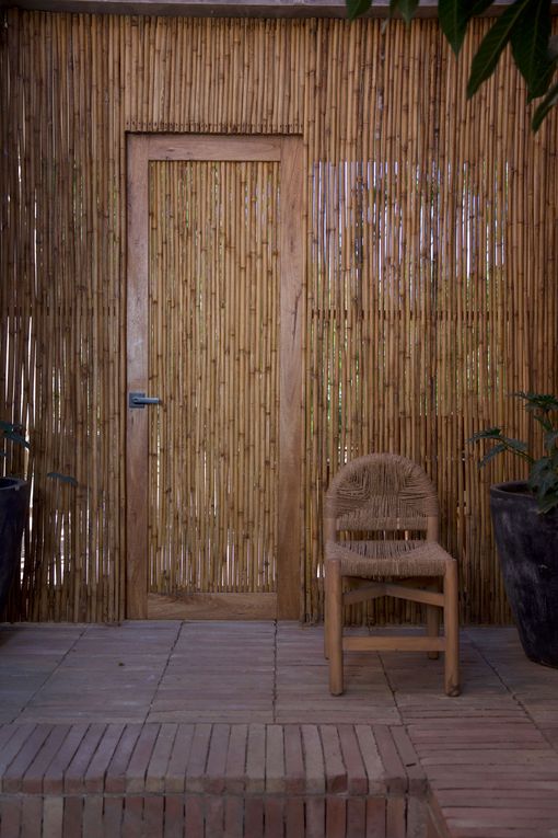 Bamboo wall with a narrow door and a wooden chair on a tiled patio.