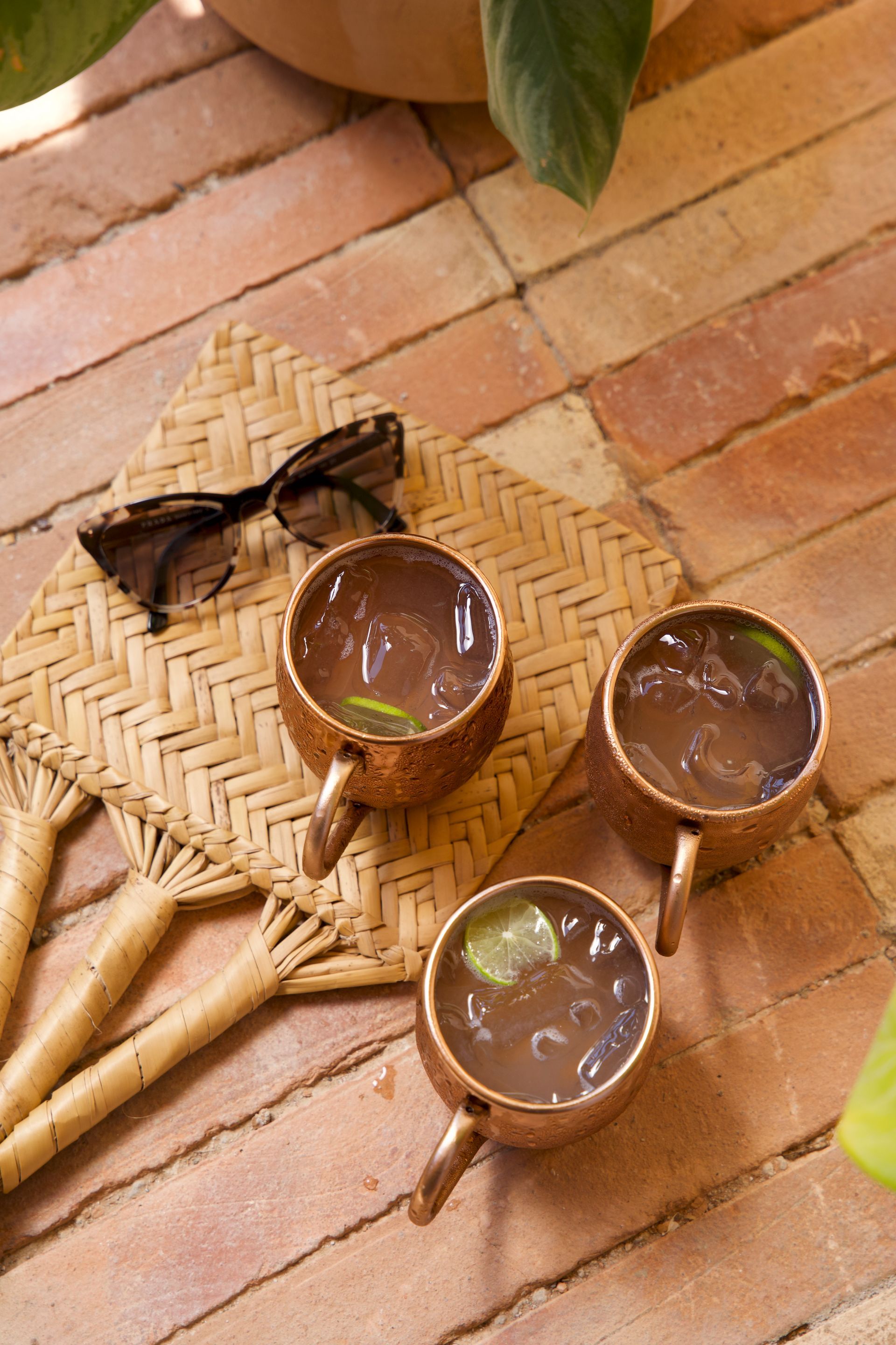 Three brass cups of tea on a woven tray over a brick floor, with a black insect beside them.