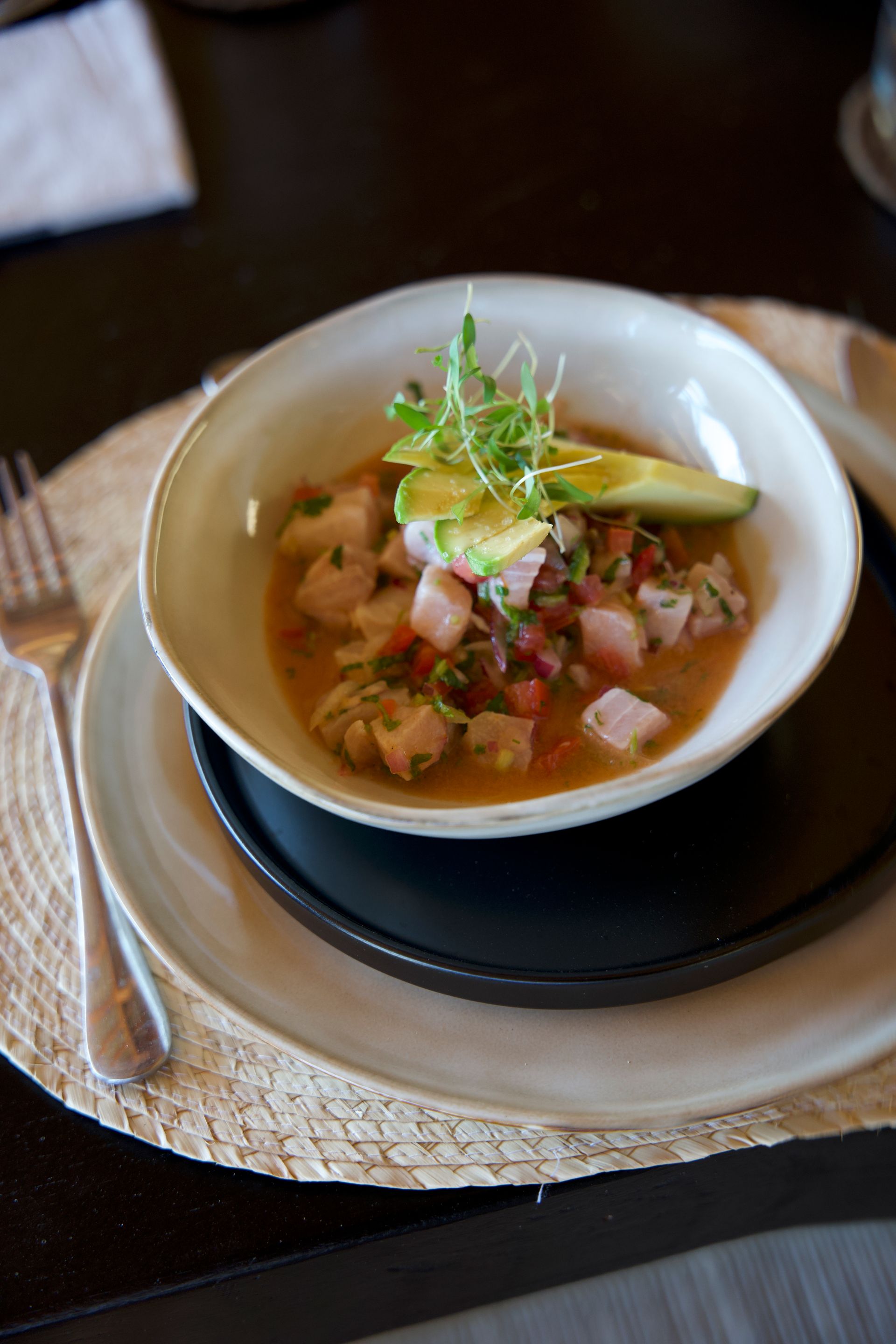 Bowl of creamy soup topped with herbs and bacon on a saucer at a dining table