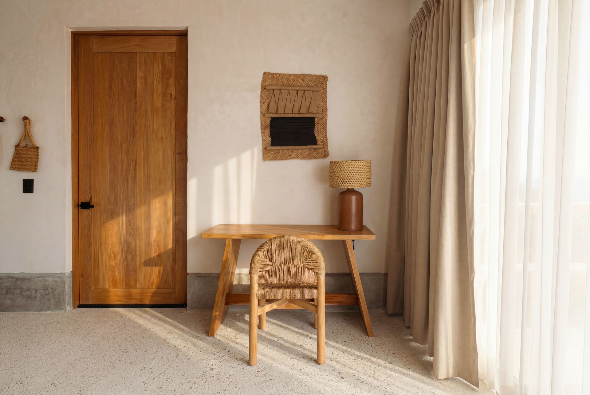 Minimal beige room with wooden door, desk, woven chair, and curtains by a bright window