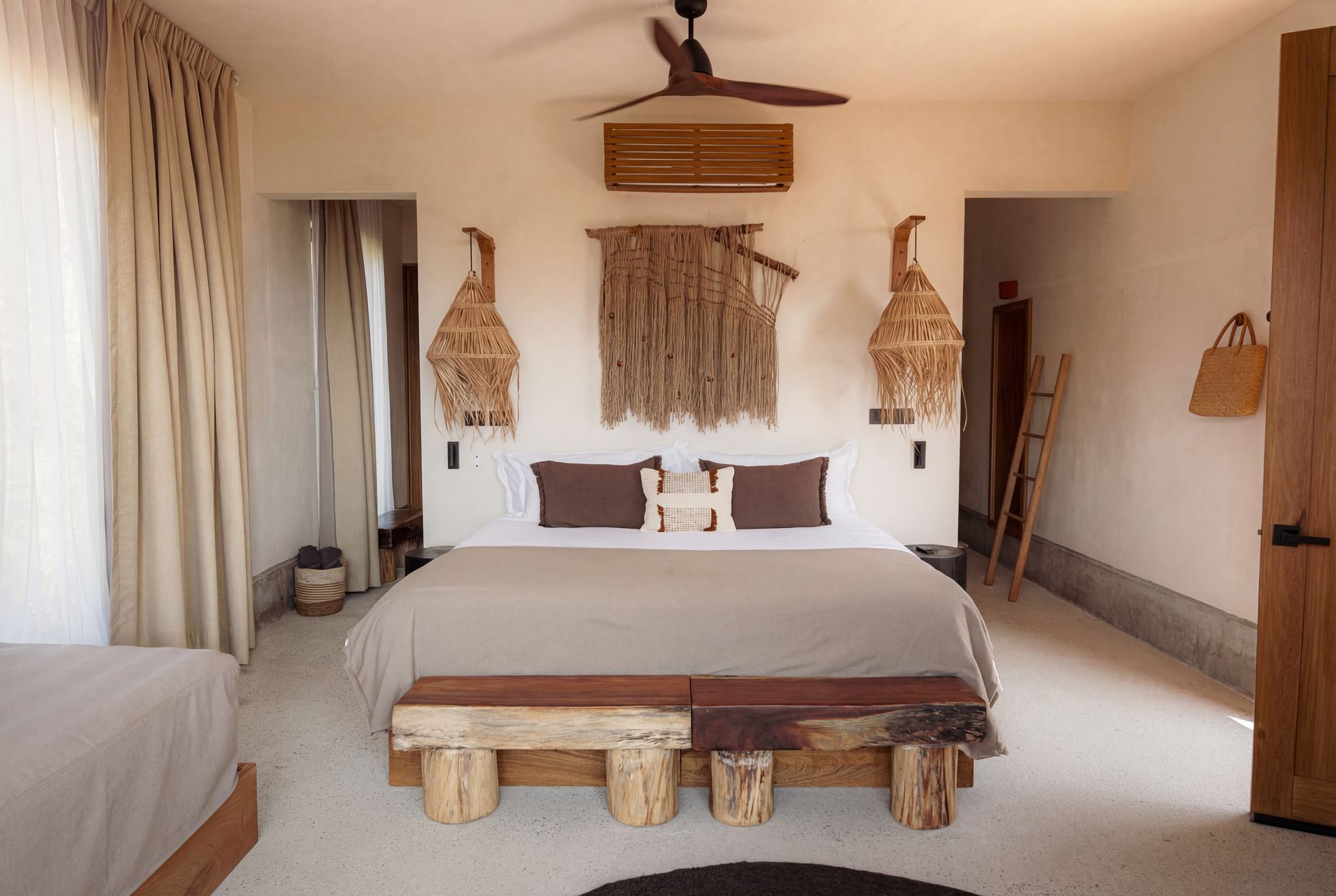 Warm beige bedroom with a large bed, woven wall decor, and natural light from the side curtains