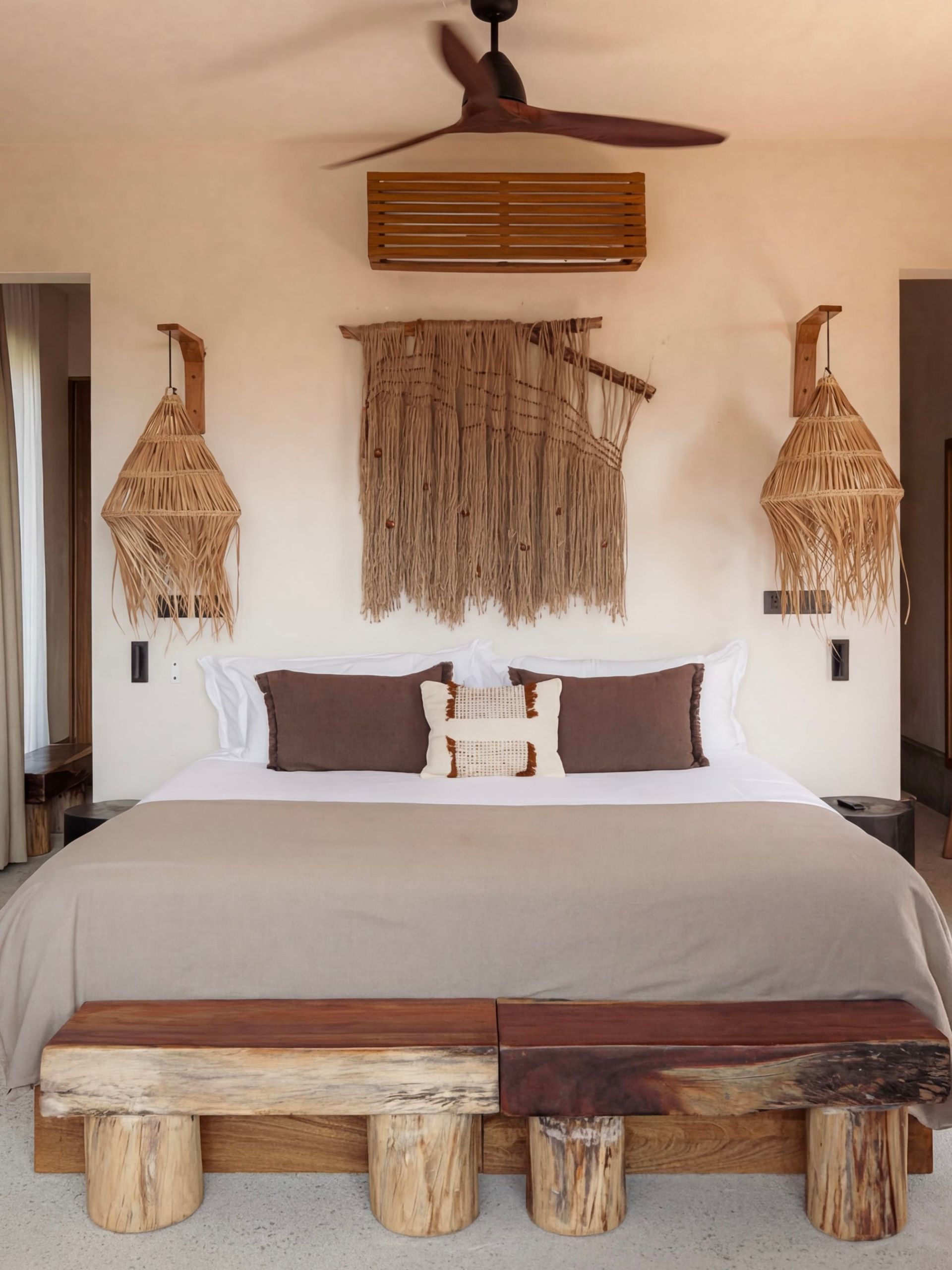 Rustic bedroom with woven wall decor, white bed, and wooden bench at the foot of the bed
