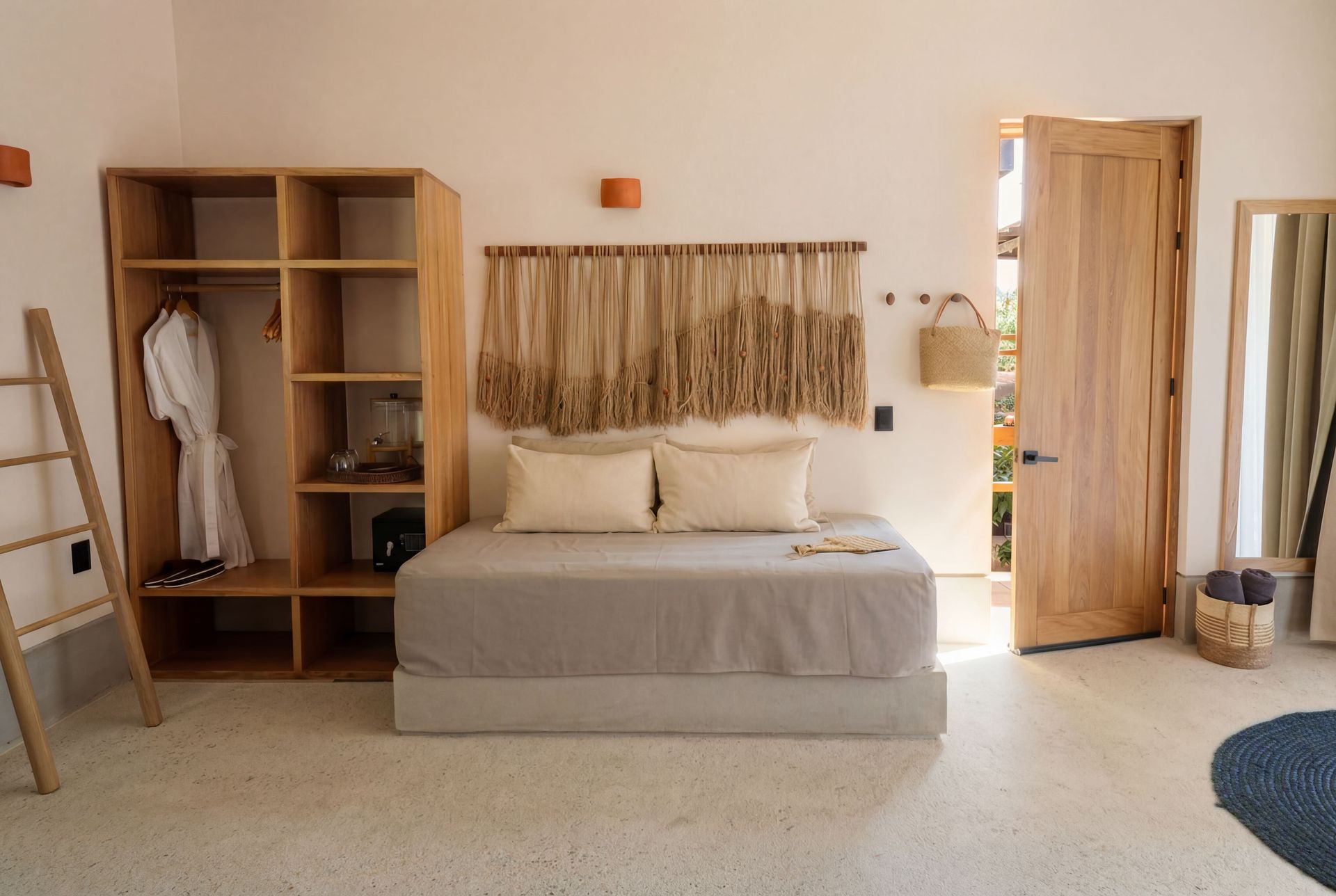 Minimalist bedroom with a wooden bed, open wardrobe, woven wall art, and a doorway to another room