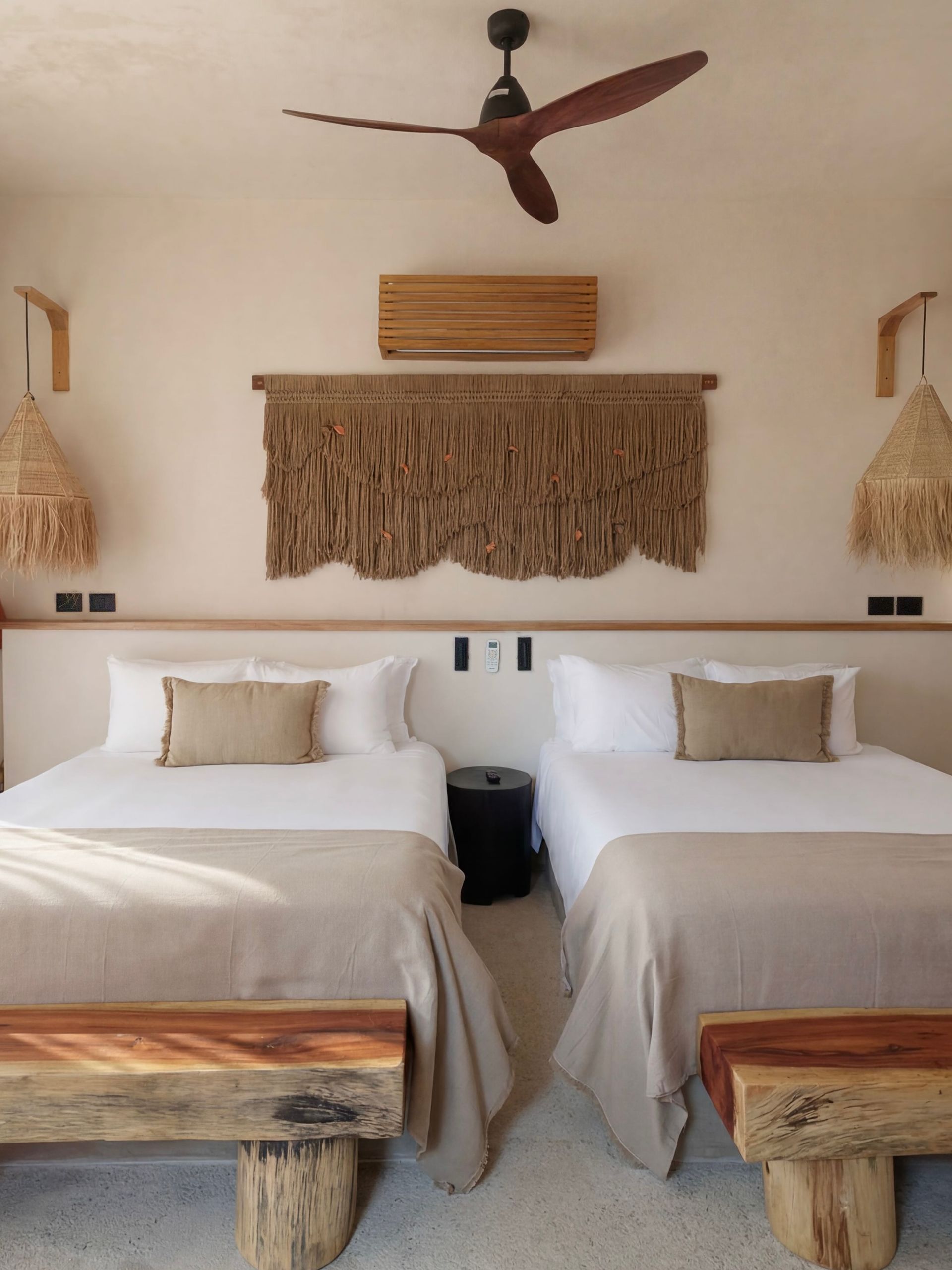 Rustic bedroom with two beds, woven wall decor, and a ceiling fan above.