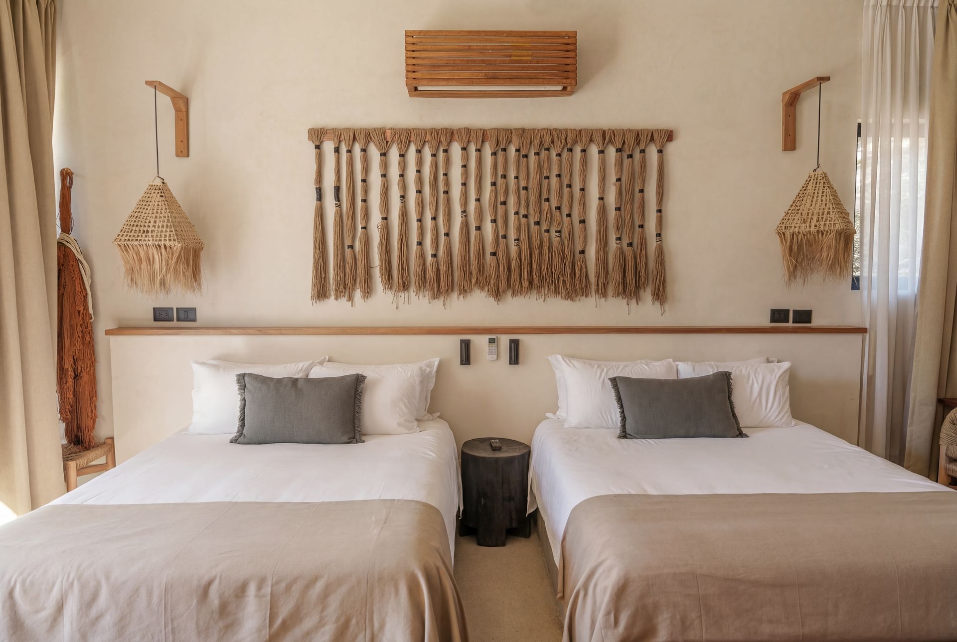 Twin beds in a beige boho-style bedroom with woven wall decor and curtains