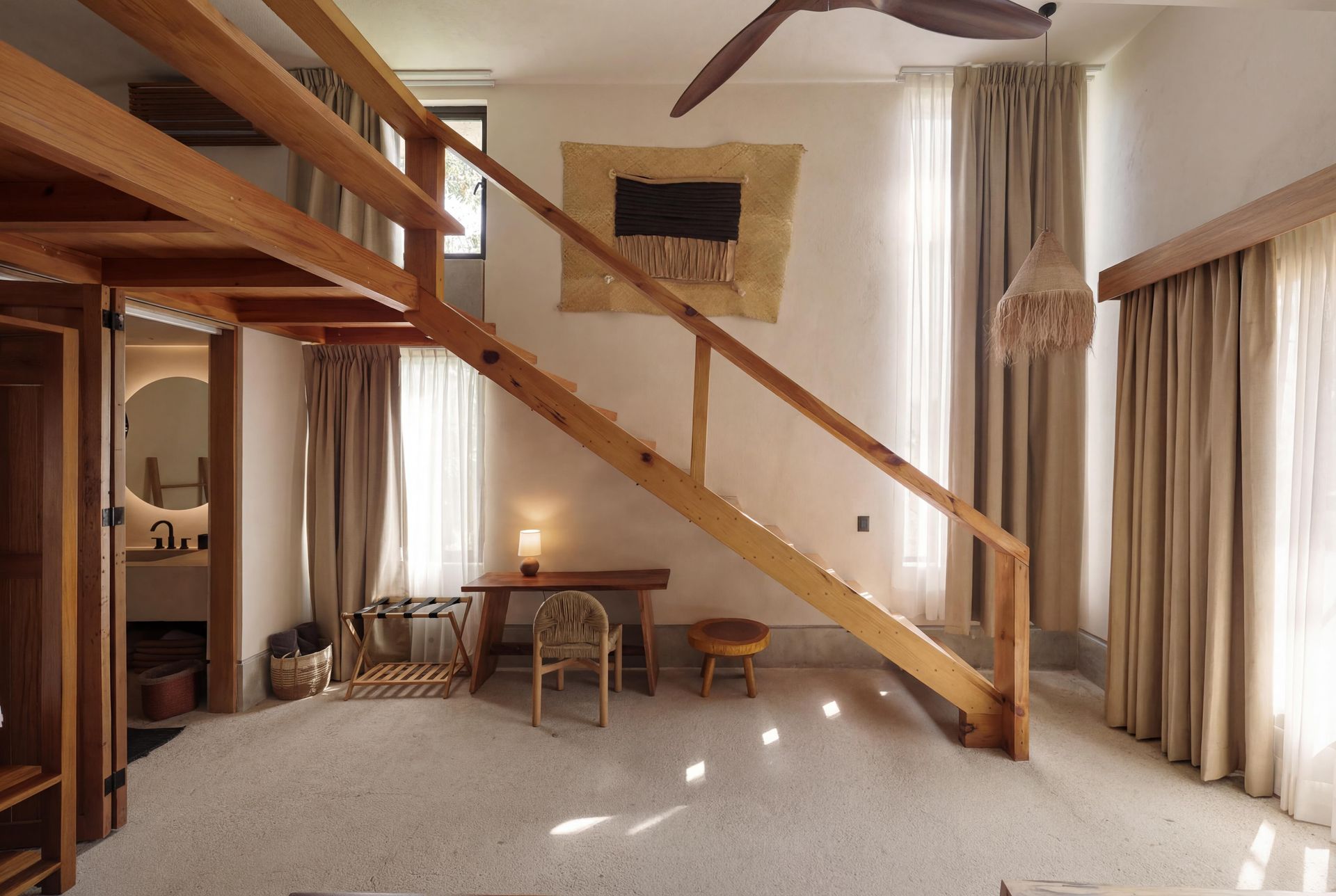Modern loft living room with wooden stairs, large windows, beige curtains, and a stone fireplace.