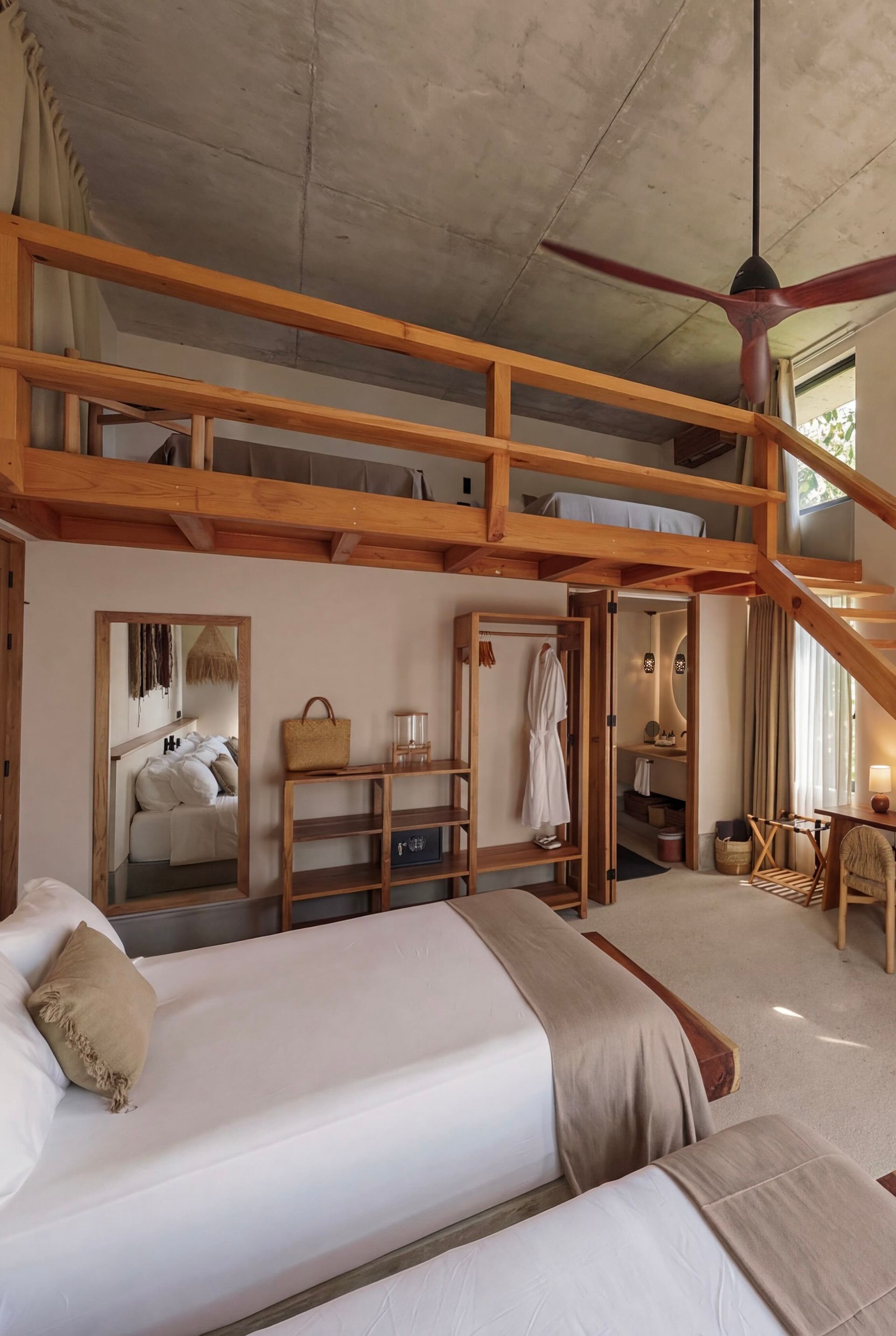Loft-style bedroom with two beds, wooden railing, and a ceiling fan in a rustic interior