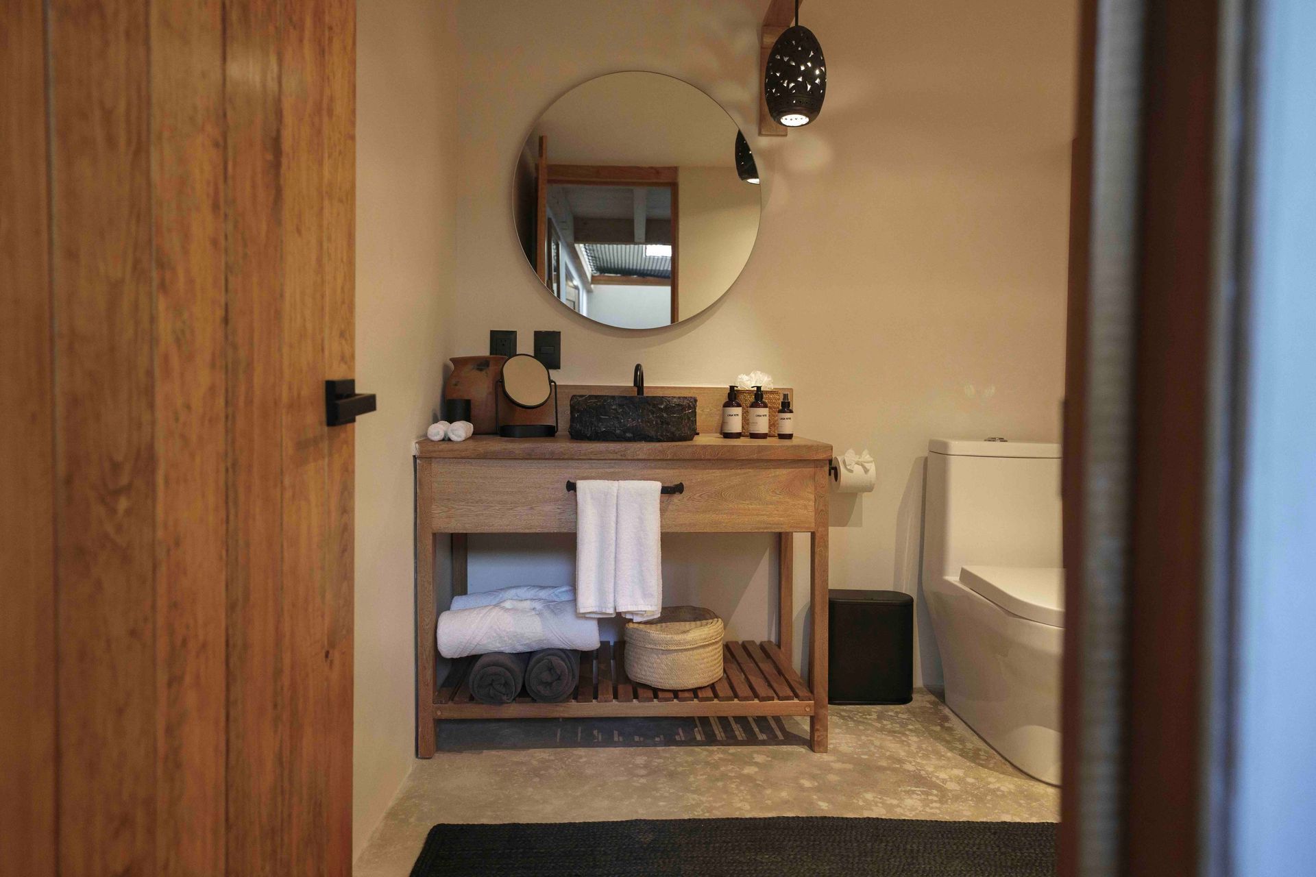 Bathroom with wooden vanity, round mirror, towels, and a bathtub in a warm-toned interior.