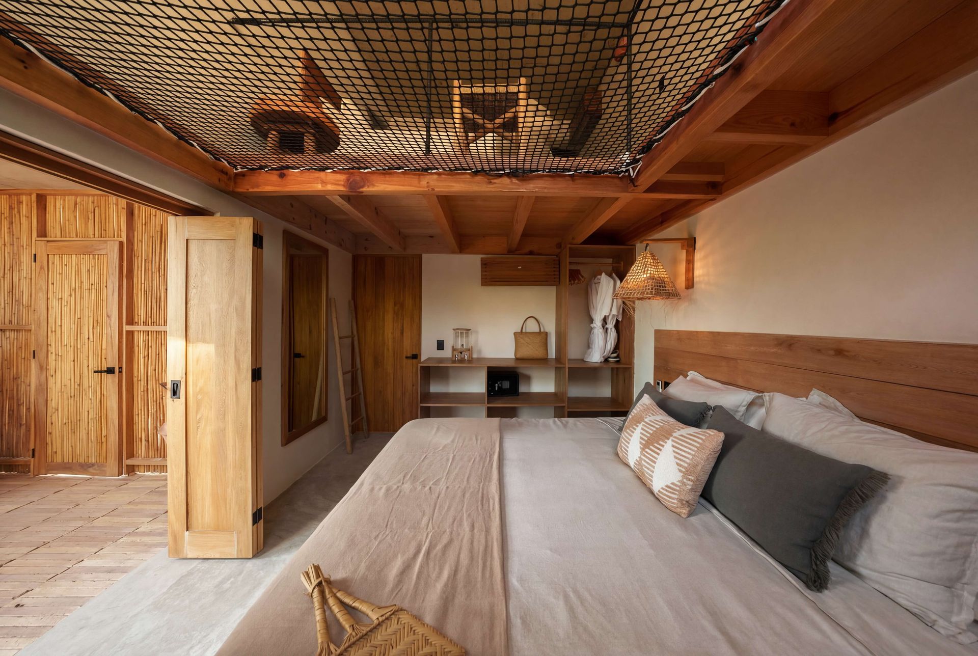 Warm bedroom with wood walls, woven ceiling light, and a king bed facing a small kitchenette.