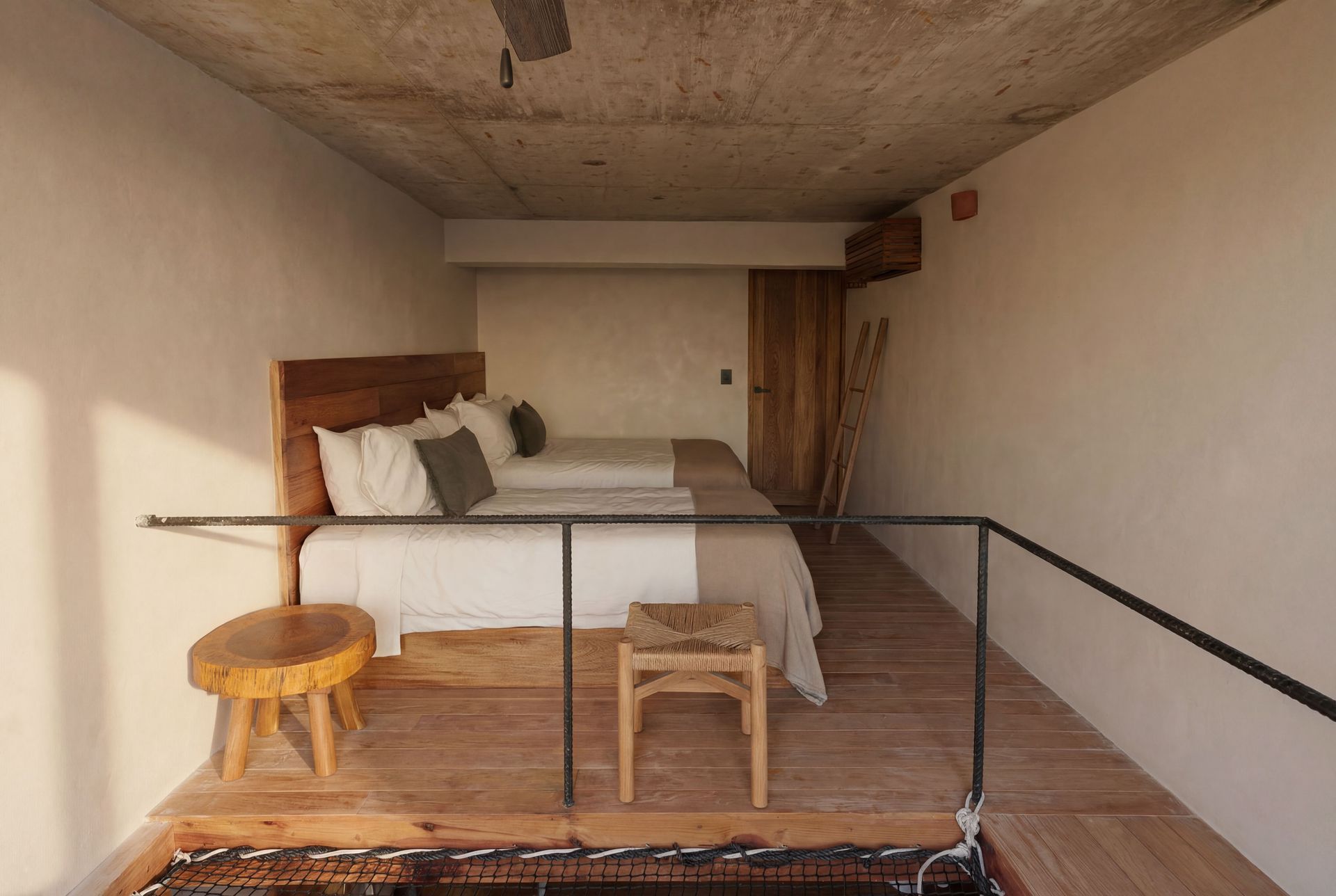 Bedroom with a bed, two stools, and a simple railing in a rustic, unfinished room