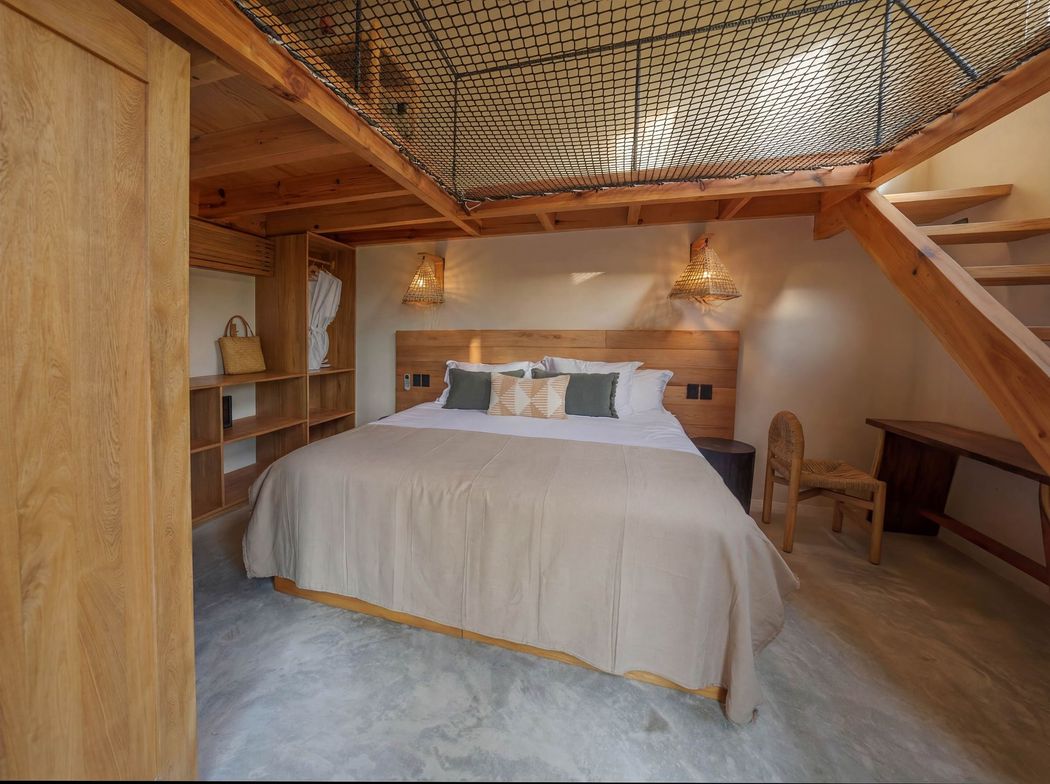 Cozy bedroom with a king bed, wood-paneled walls, ladder shelf, and carved ceiling detail.