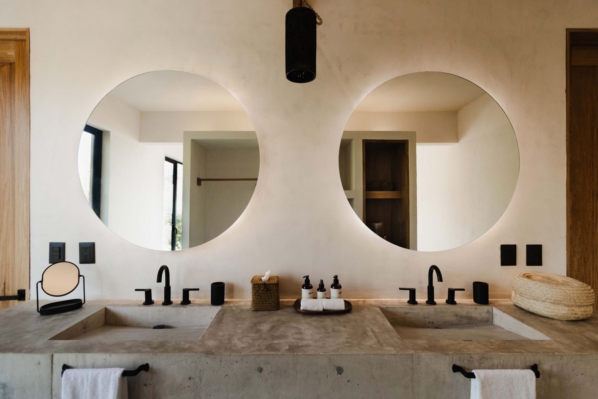 Modern double-sink bathroom vanity with large round mirrors, stone countertop, and black fixtures.