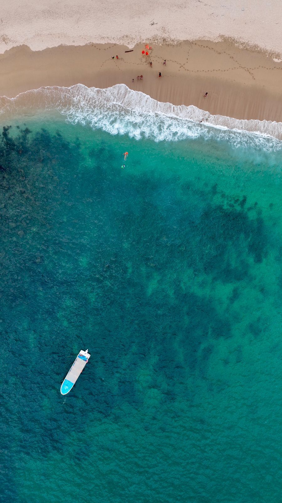 Aerial view of a sandy beach meeting turquoise water, with a small boat floating near shore.