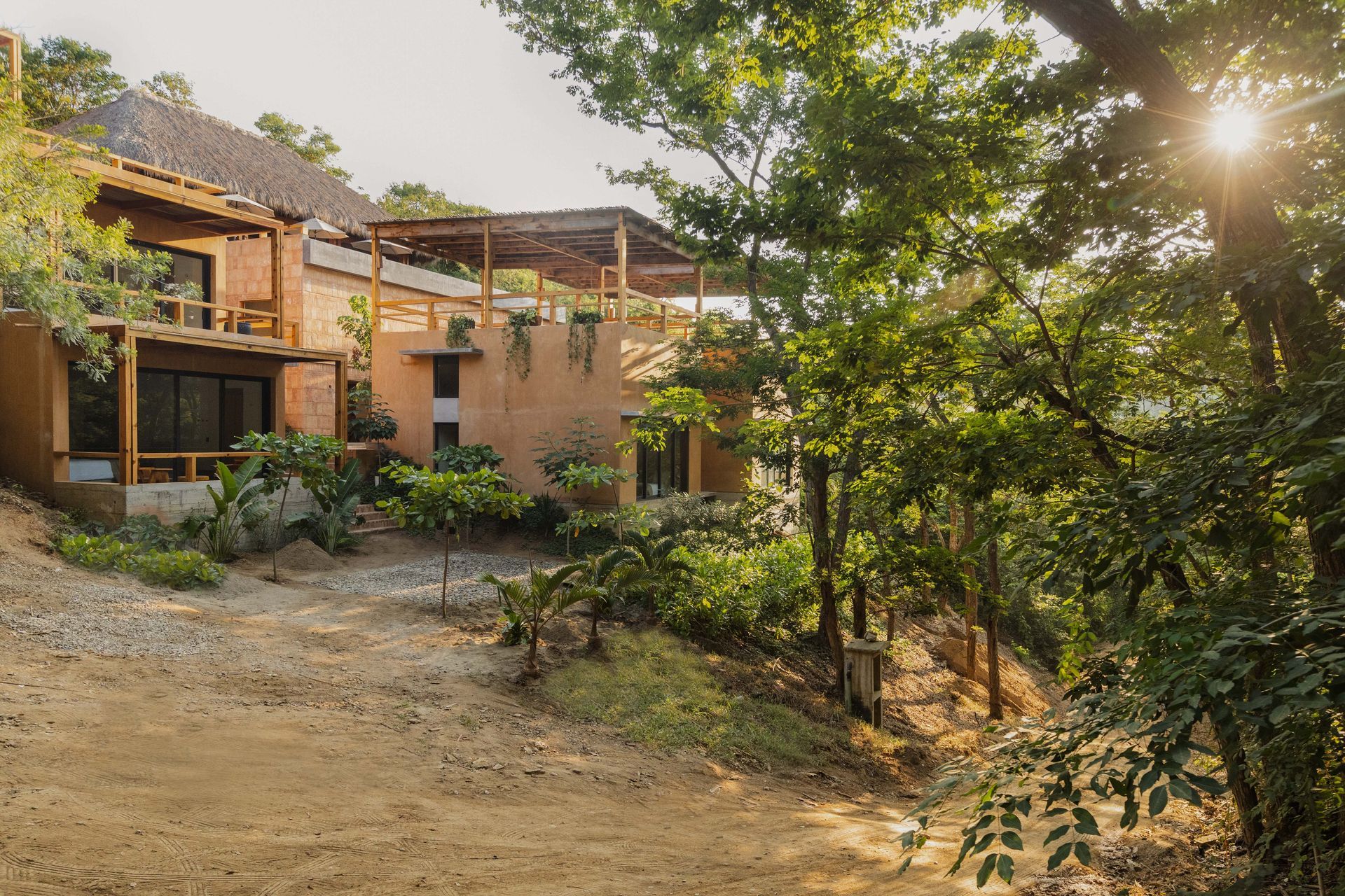 Sunlit rustic house with terracotta walls, garden, and dirt path surrounded by trees