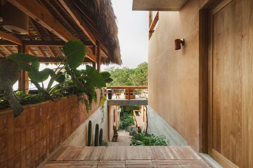 Wooden stairs between tan walls lead to a tropical courtyard with lush green plants and a covered balcony.
