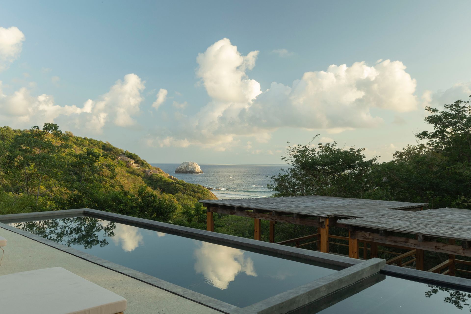 Oceanview patio with a reflecting pool, lush greenery, and a cloudy sky at sunset