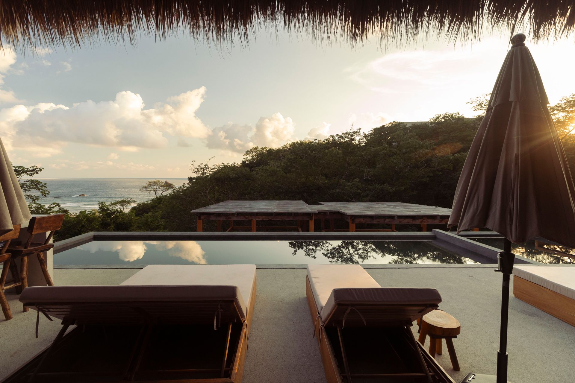 Resort terrace with lounge chairs and infinity pool overlooking the ocean at sunset