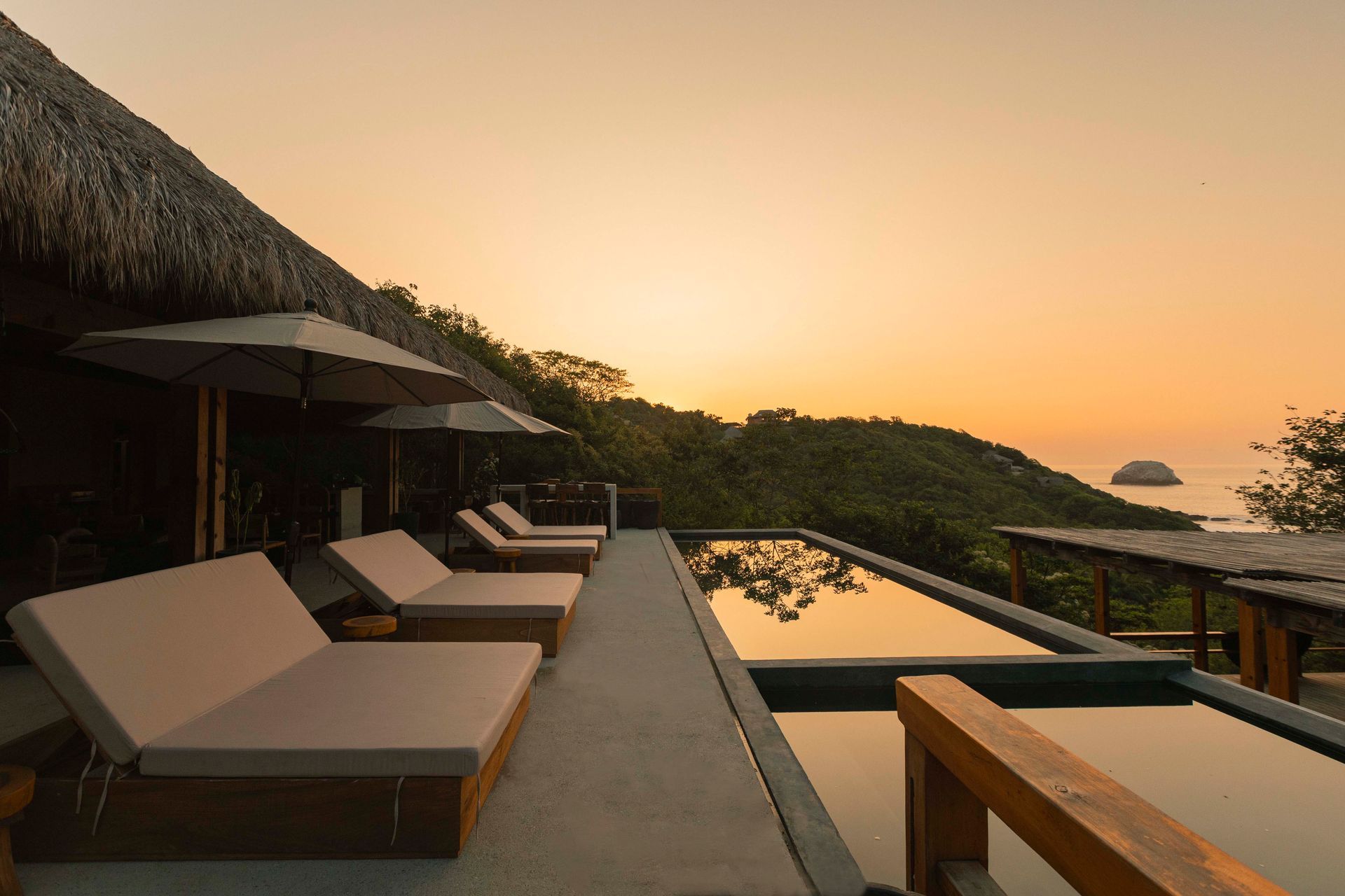 Luxury resort deck with loungers and umbrellas beside an infinity pool at sunset, overlooking the ocean