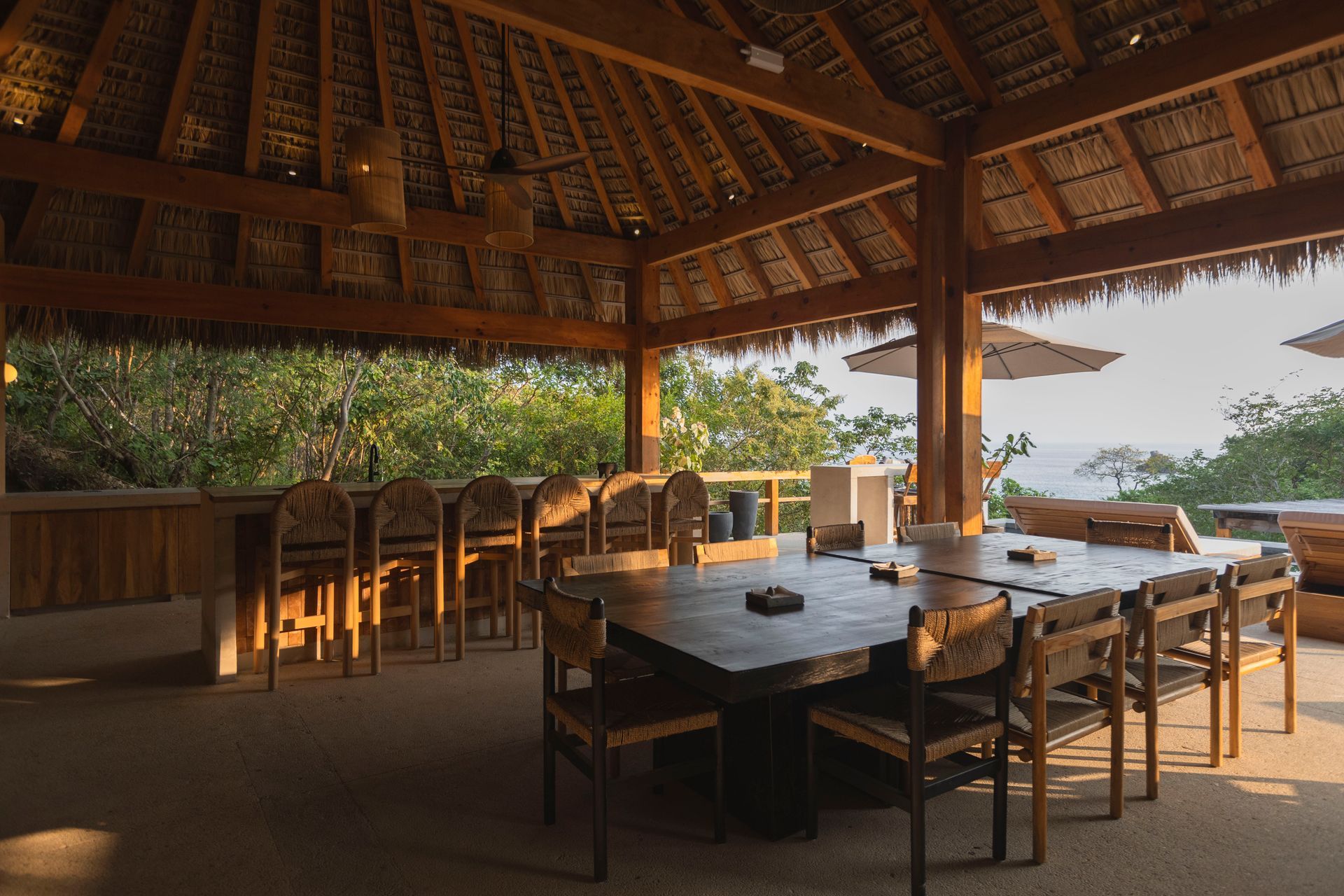 Open-air wooden dining pavilion with tables, chairs, and warm sunset light overlooking greenery and water