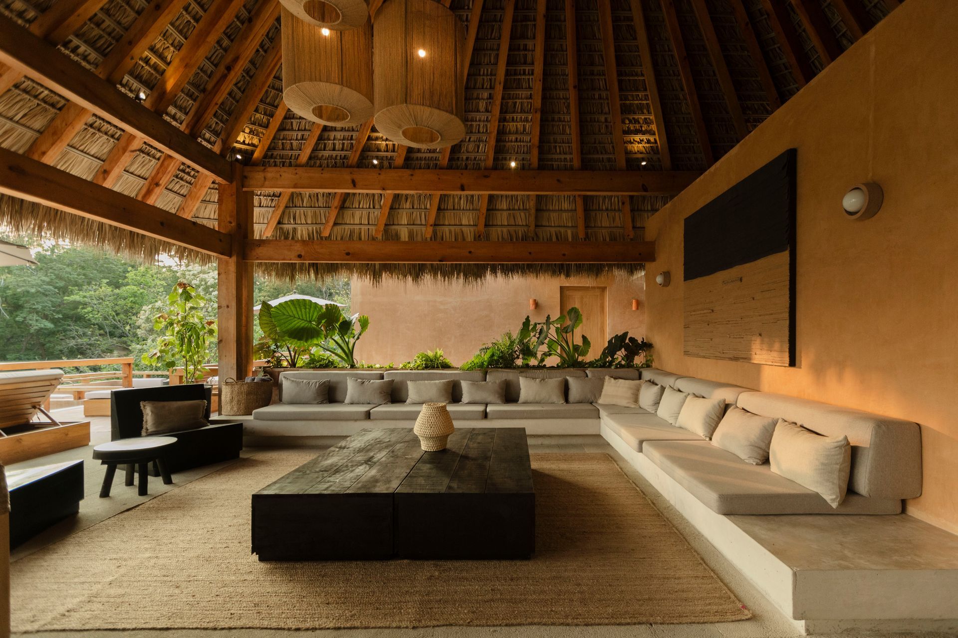 Open-air living room with beige sofas, low table, warm wood ceiling, and garden views