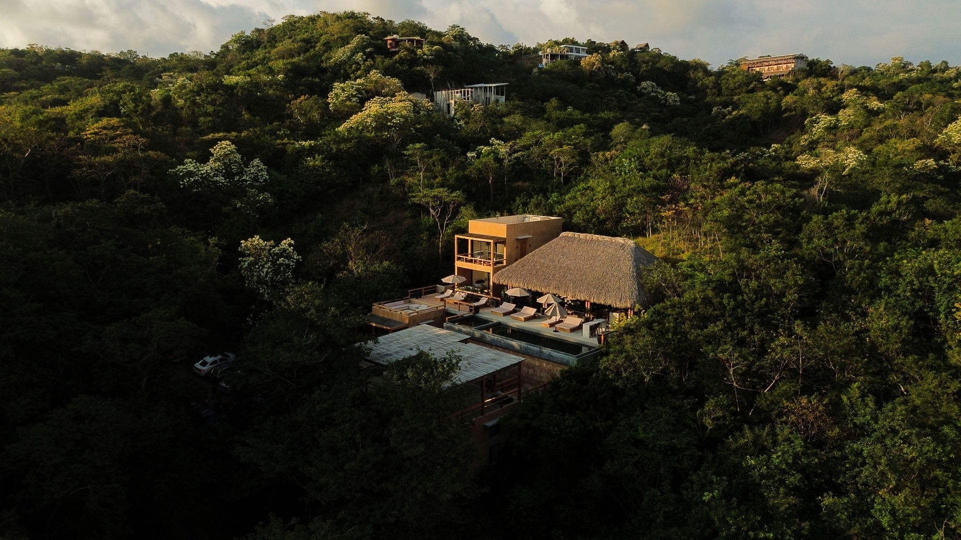 A small thatched-roof house nestled in dense green forest at sunset