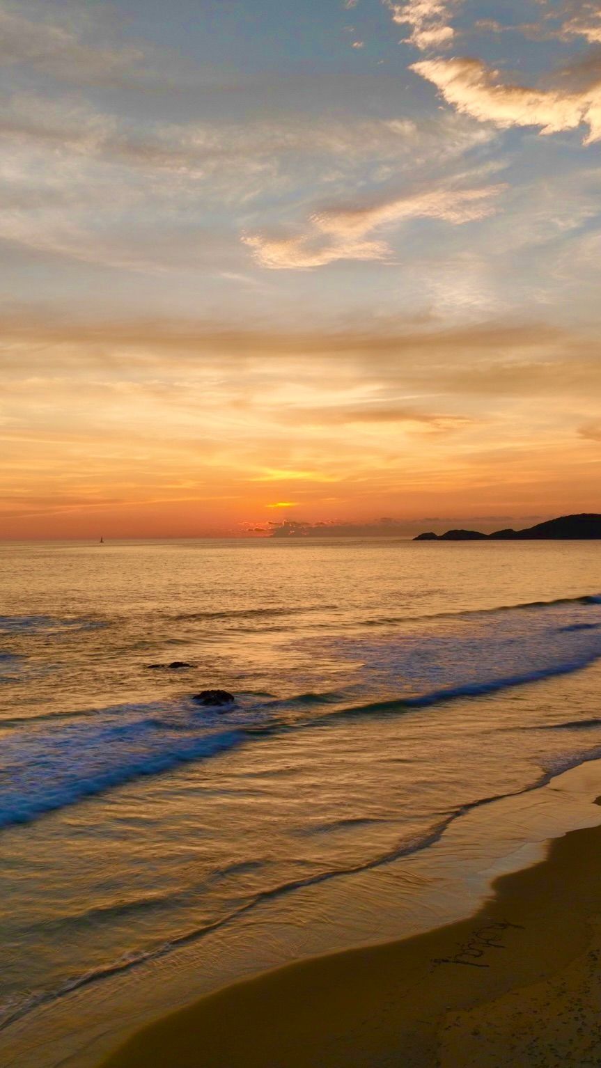 Sunset over a calm beach with orange sky, gentle waves, and dark shoreline