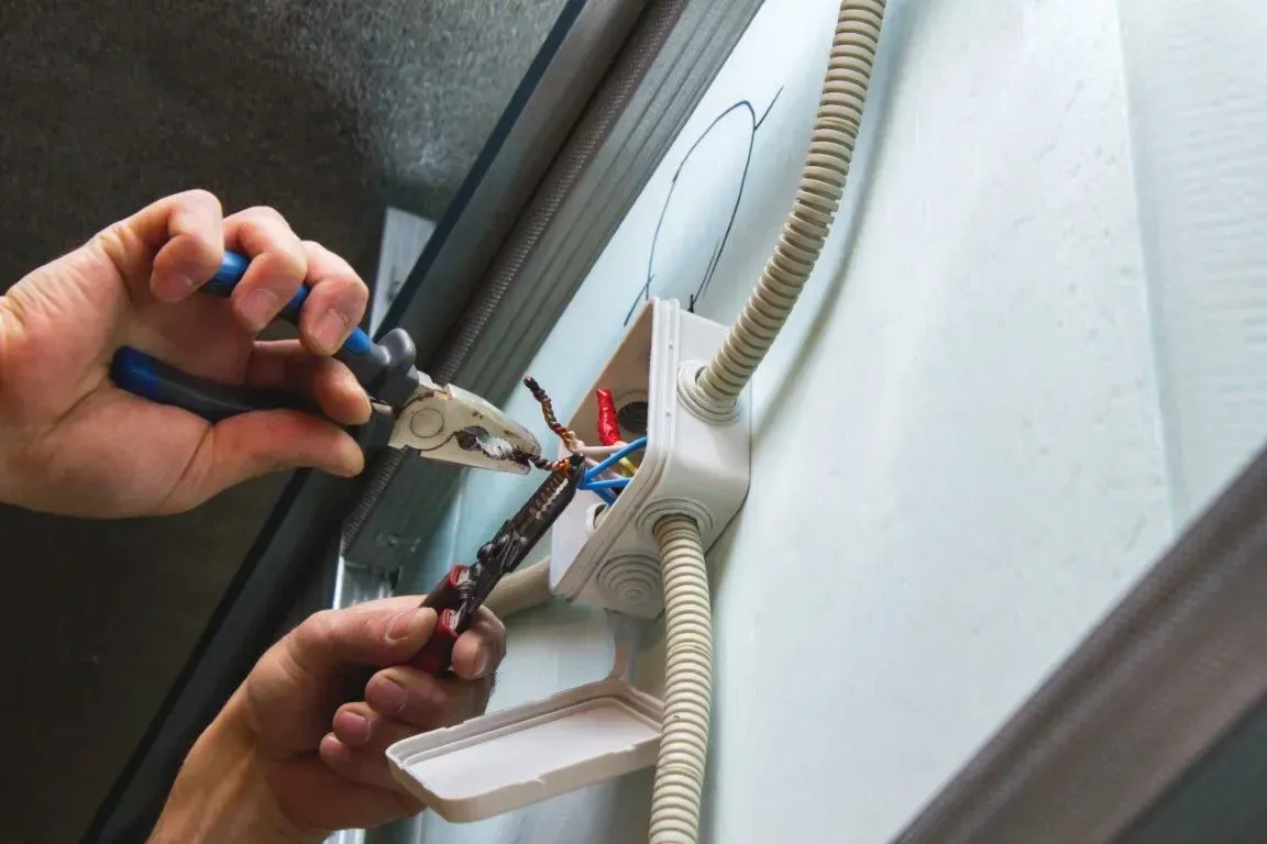 Hands using pliers to work on electrical wiring inside a wall-mounted junction box.