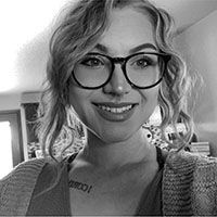 Woman with curly hair and glasses smiling at the camera, wearing a sweater.