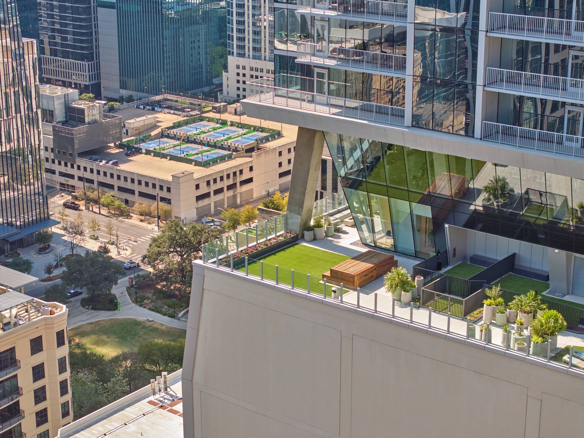 High-angle view of a modern building rooftop with a grassy area, trees, and city skyline.