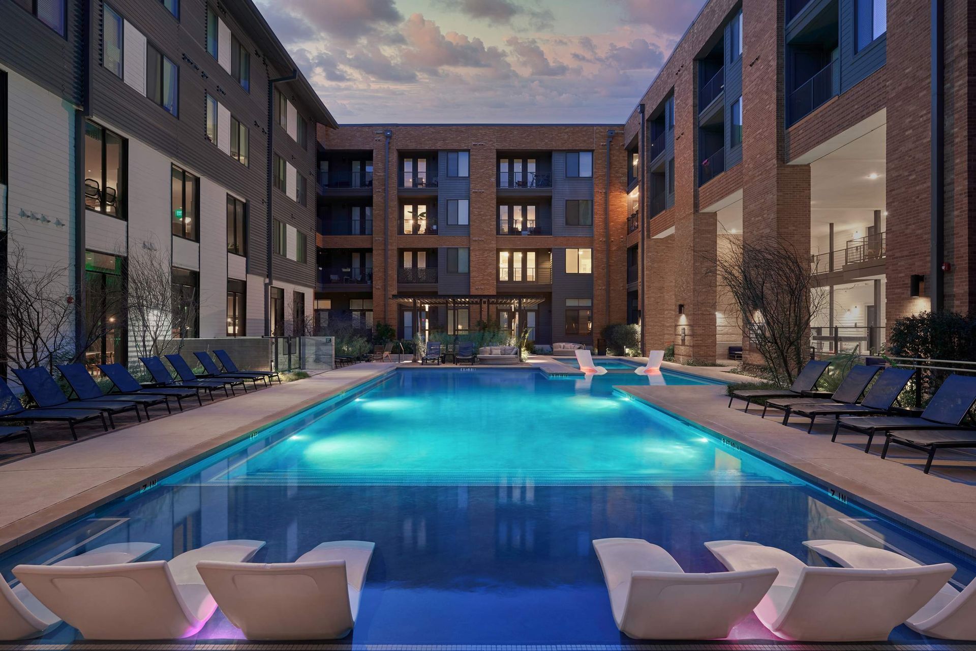 An outdoor pool area at an apartment complex with lounge chairs and buildings.