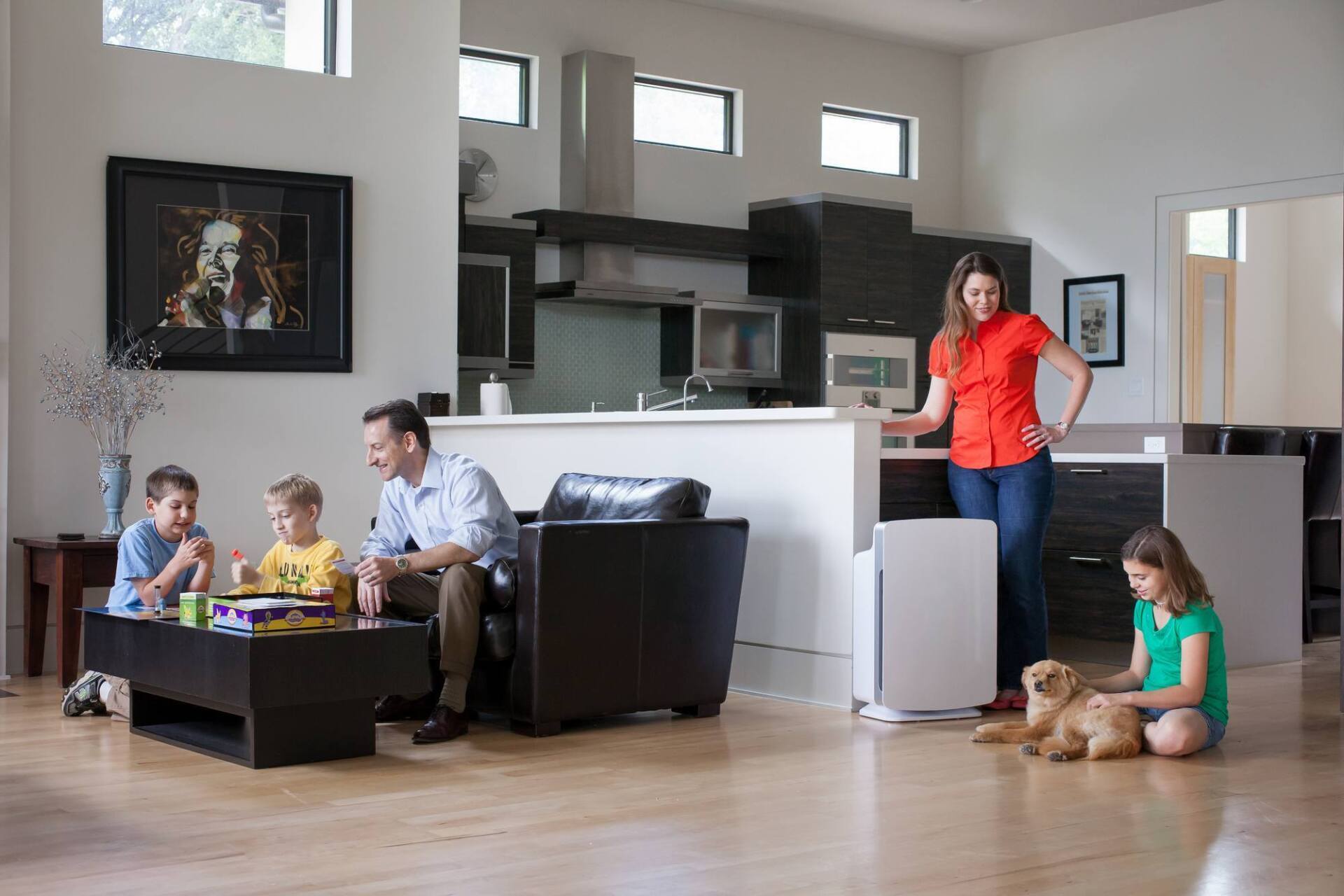 Family in living room; mother at air purifier, father & children at table with dog.