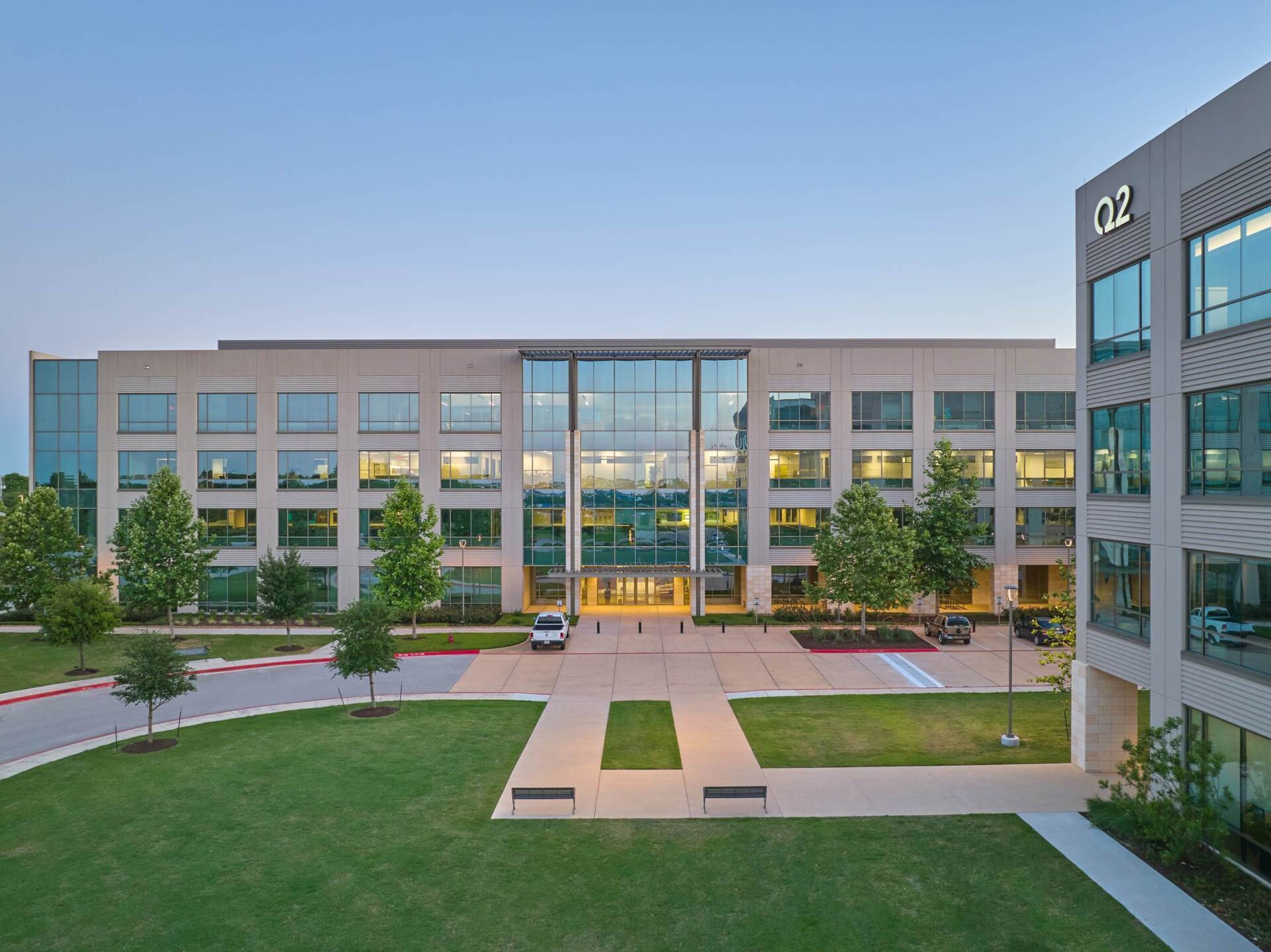 Office building exterior with glass entrance, trees, and green lawn.