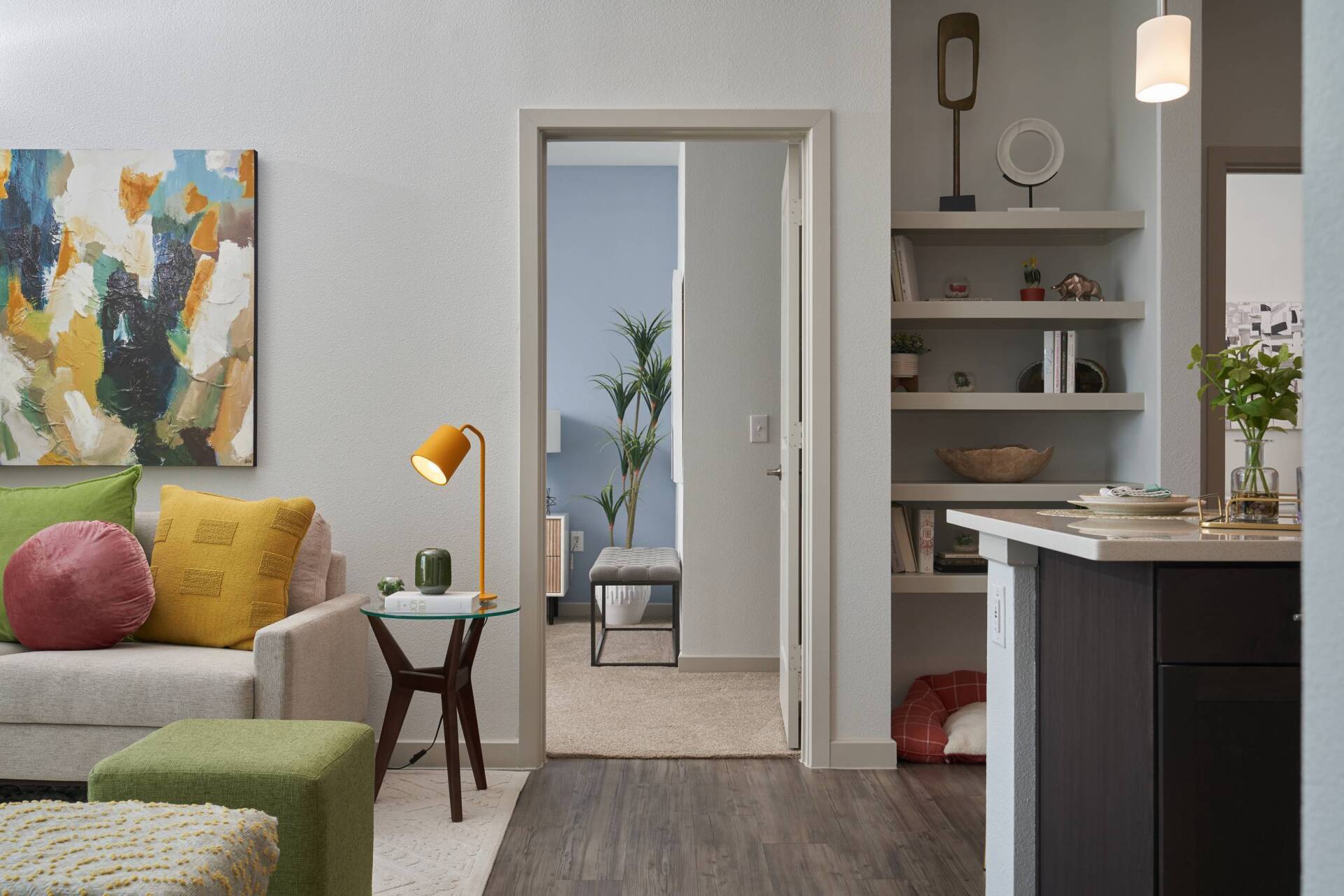 Cozy living room with a couch, art, and a view into a hallway.  A modern lamp and shelves are visible.