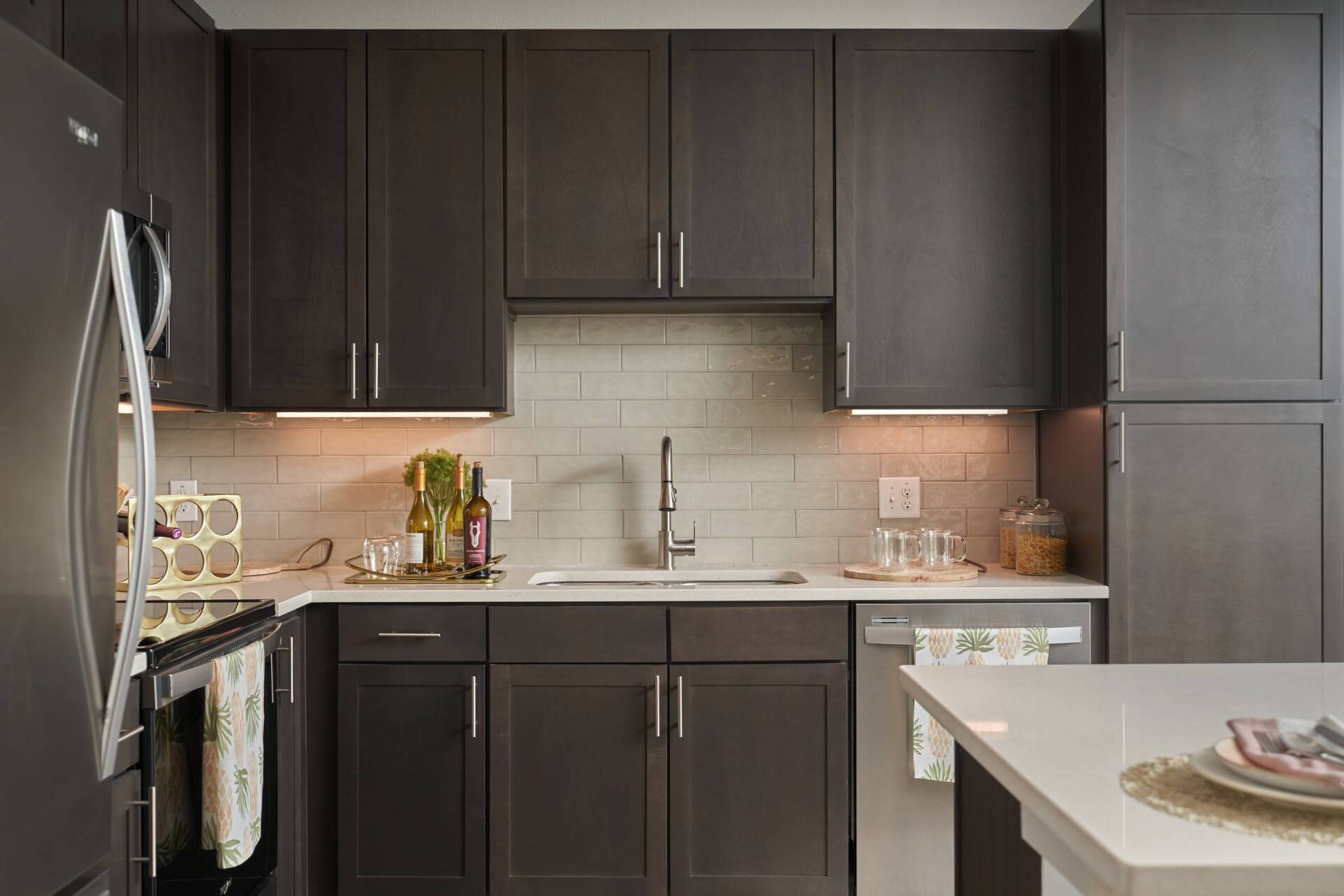 Dark brown kitchen cabinets with white countertops, sink, and backsplash.