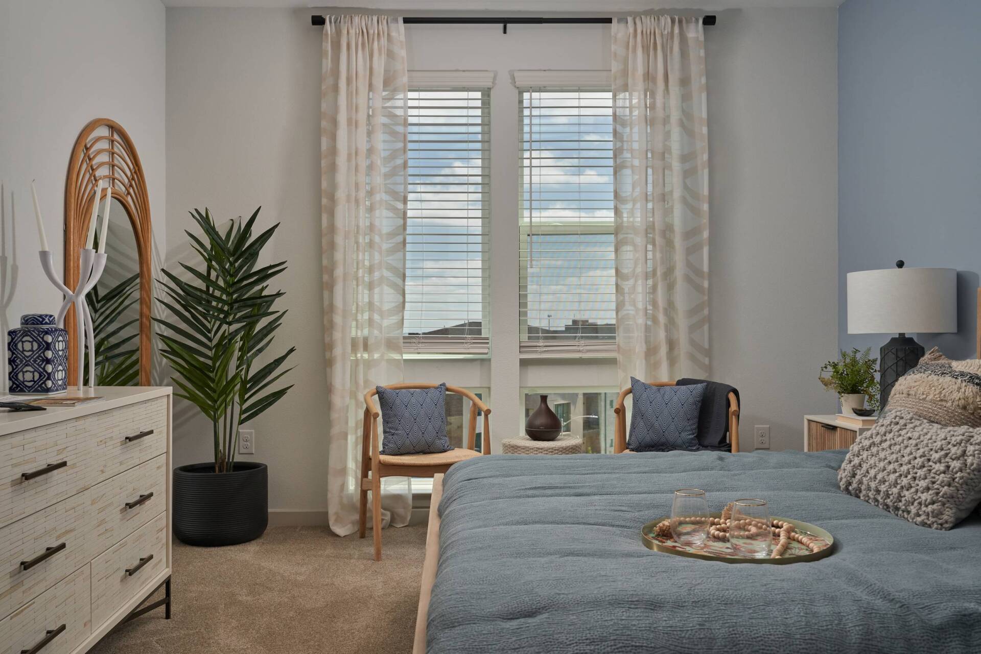Bedroom with blue and white decor, large window, potted plant, dresser, and bed.