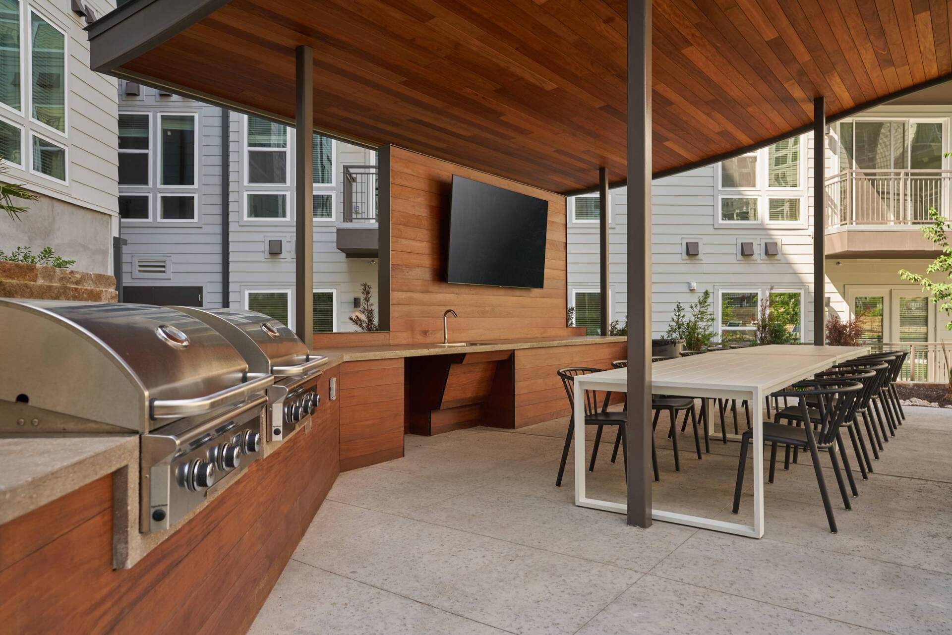 Outdoor kitchen with grill, table, chairs, TV, and wooden canopy.