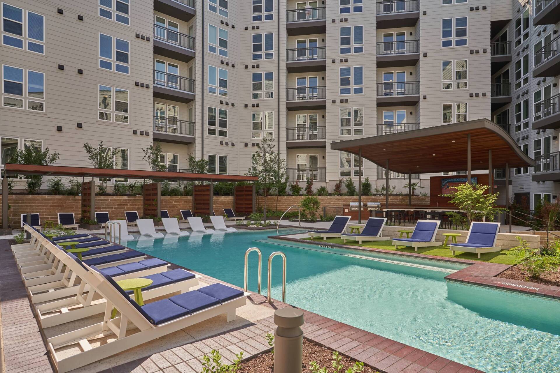 Swimming pool with lounge chairs, next to an apartment building.