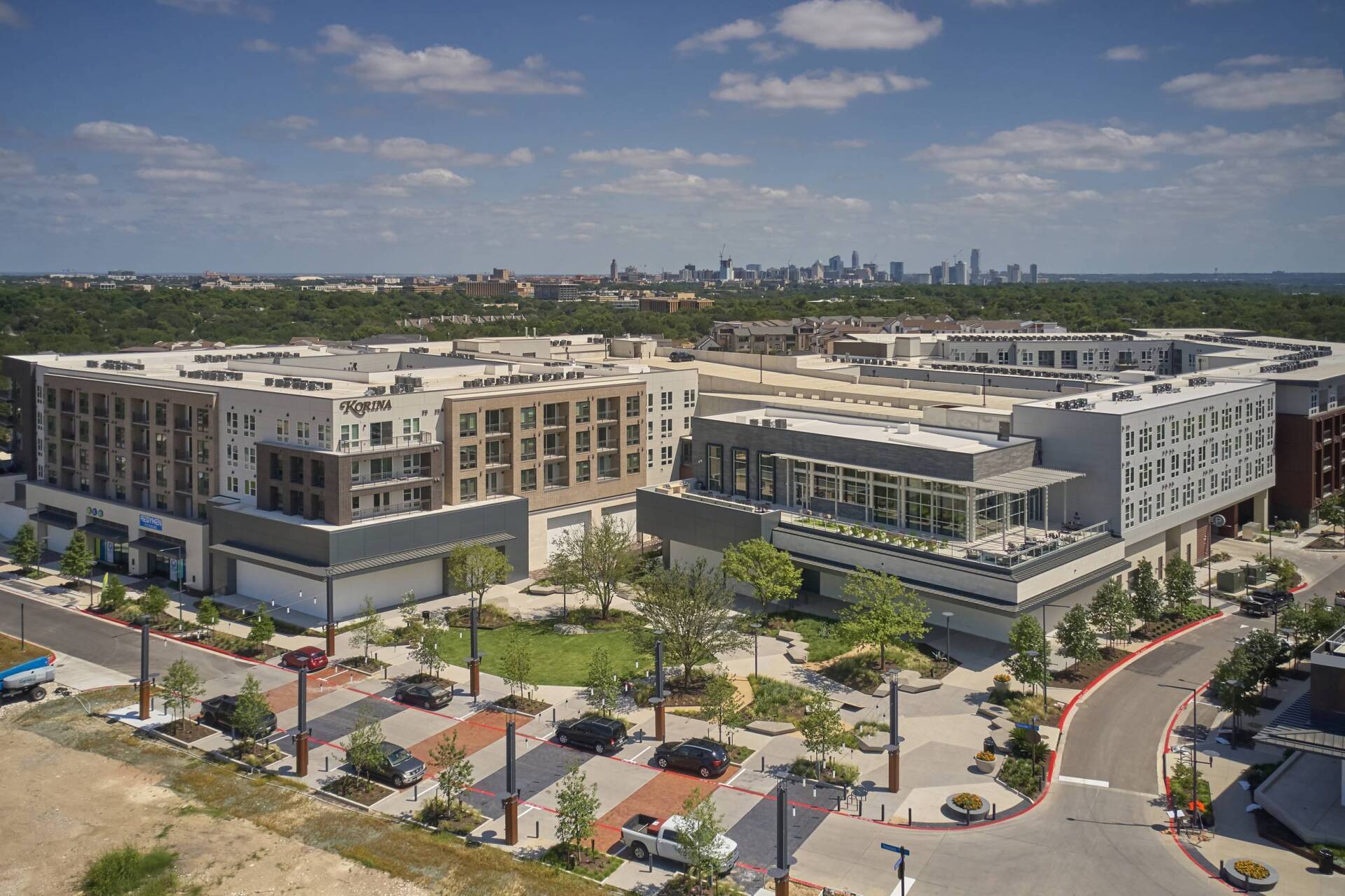 Aerial view of multi-building complex with green space, city skyline in the distance, sunny day.