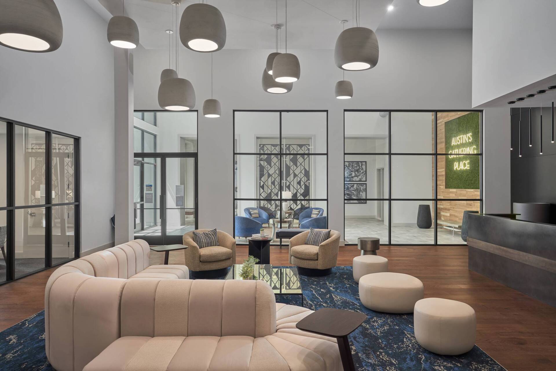 Lobby with modern furniture, blue rug, glass walls, and pendant lights. A sign reads 