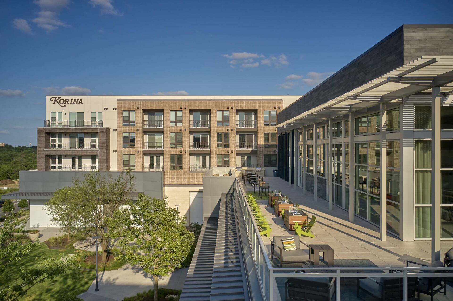 Modern apartment building with outdoor patio and greenery under a blue sky.