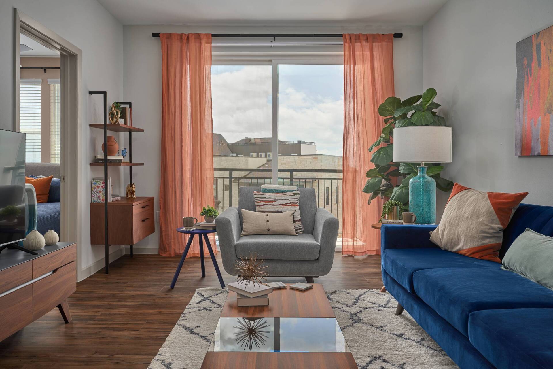 Living room with blue sofa, gray armchair, peach curtains, and wooden furniture.