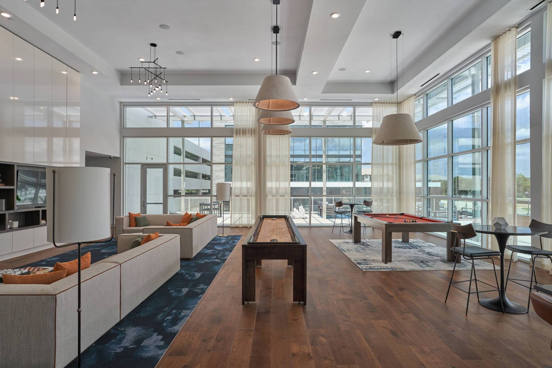 Spacious lounge with large windows, sofas, shuffleboard, and pool table. Natural light and neutral tones.