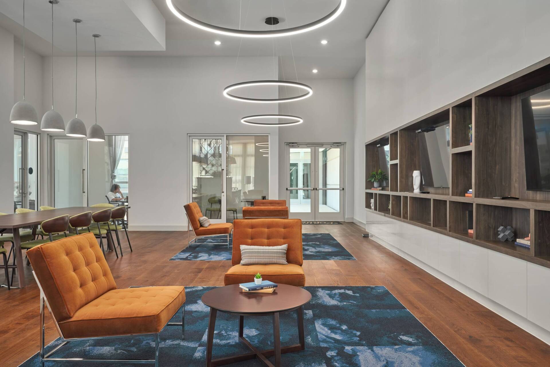 Modern lounge area with orange chairs, wood shelving, and large circular lights.