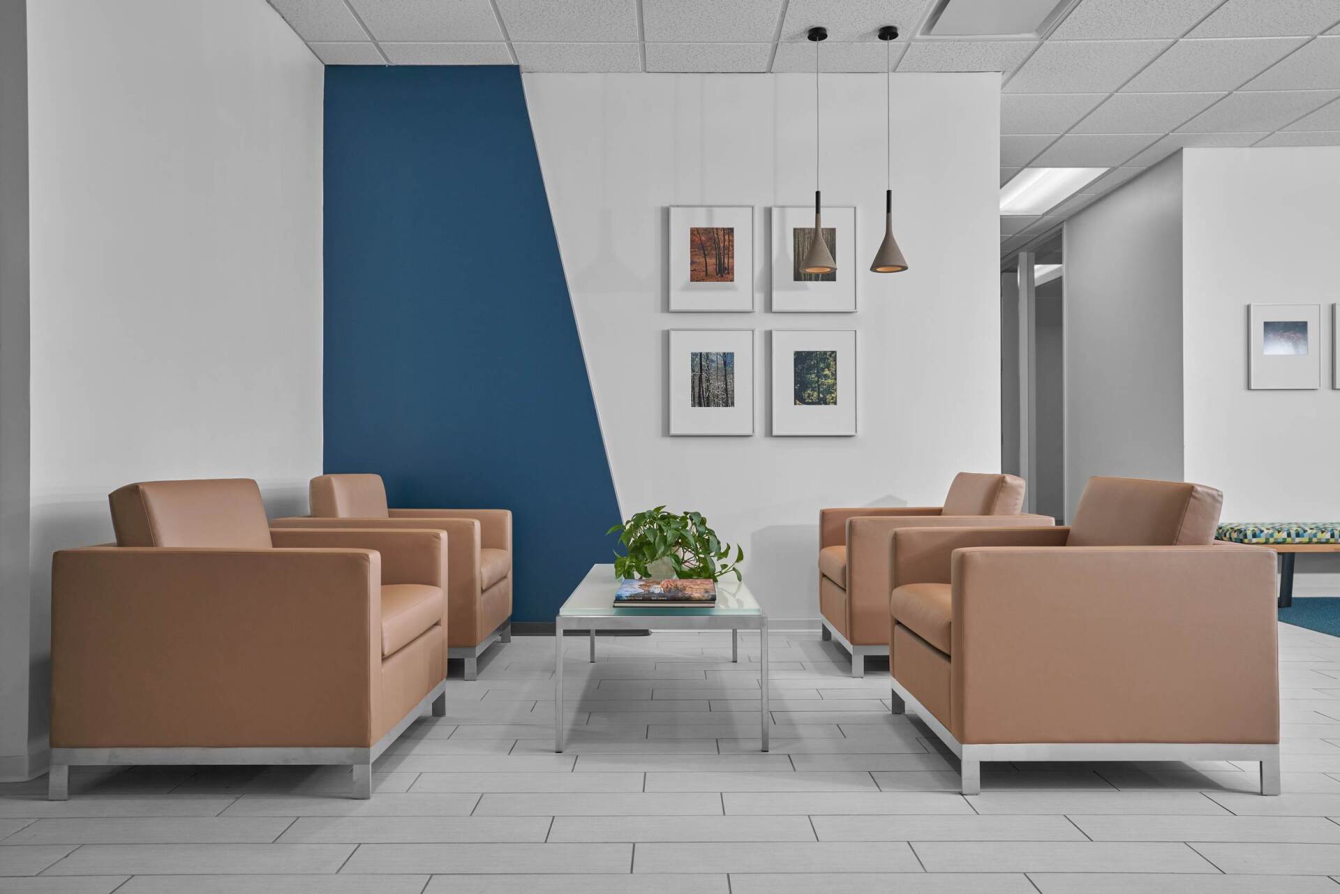 Reception area with tan armchairs, white walls, and blue accent. Four framed pictures and a small table.