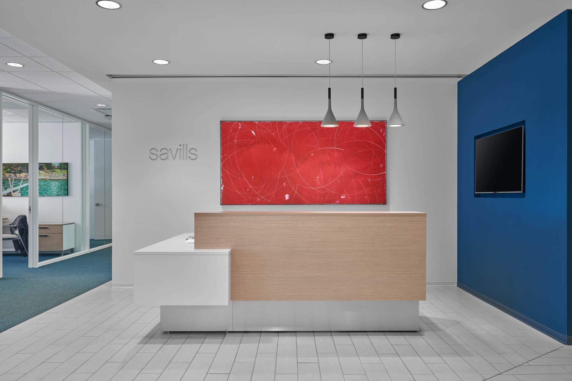 Modern office reception area with a wooden desk, red artwork, and blue accent wall.