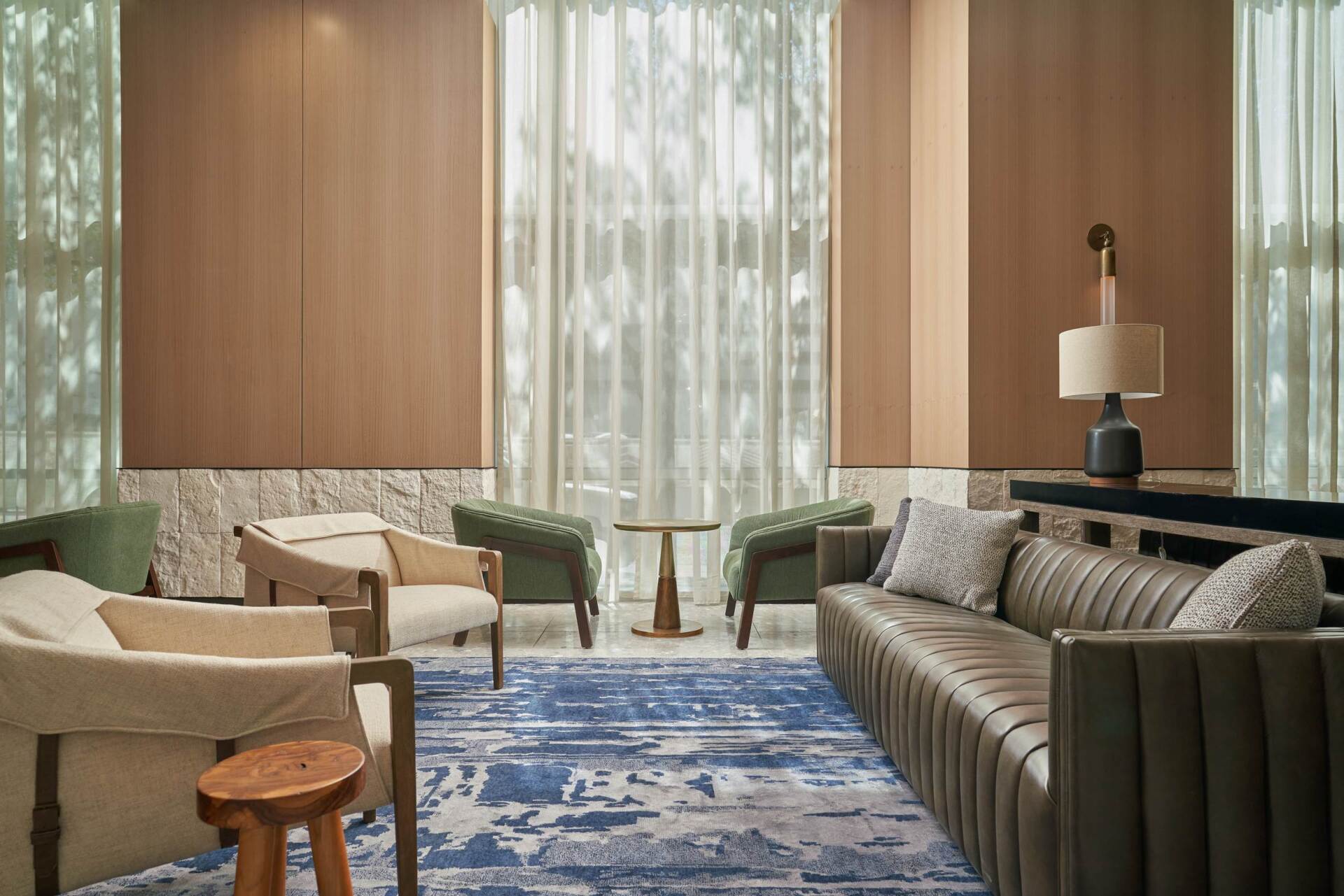 Cozy lounge area with light-colored chairs, sofa, and a blue rug in front of a large window.