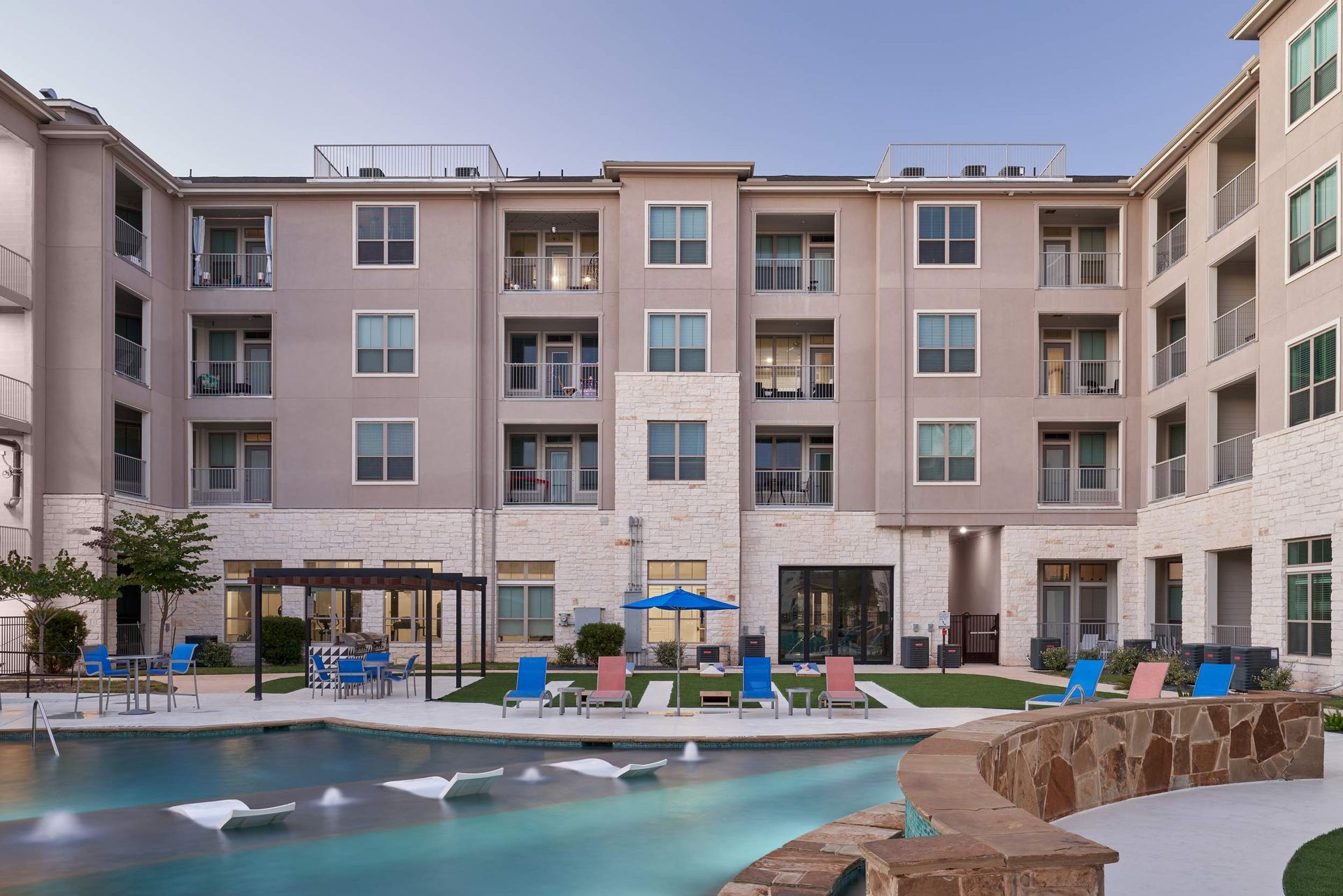 Apartment complex with a swimming pool and lounge chairs. Exterior view in the evening light.